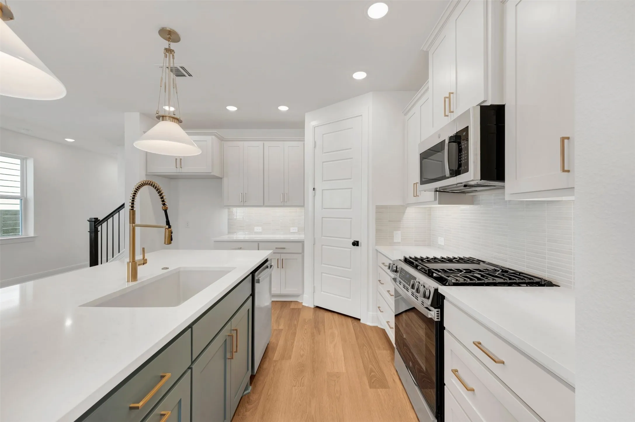 Modern kitchen featuring a white subway tile backsplash, stainless steel appliances, white cabinetry, a kitchen island with an integrated sink and gold-finish fixtures, and wood-finish flooring