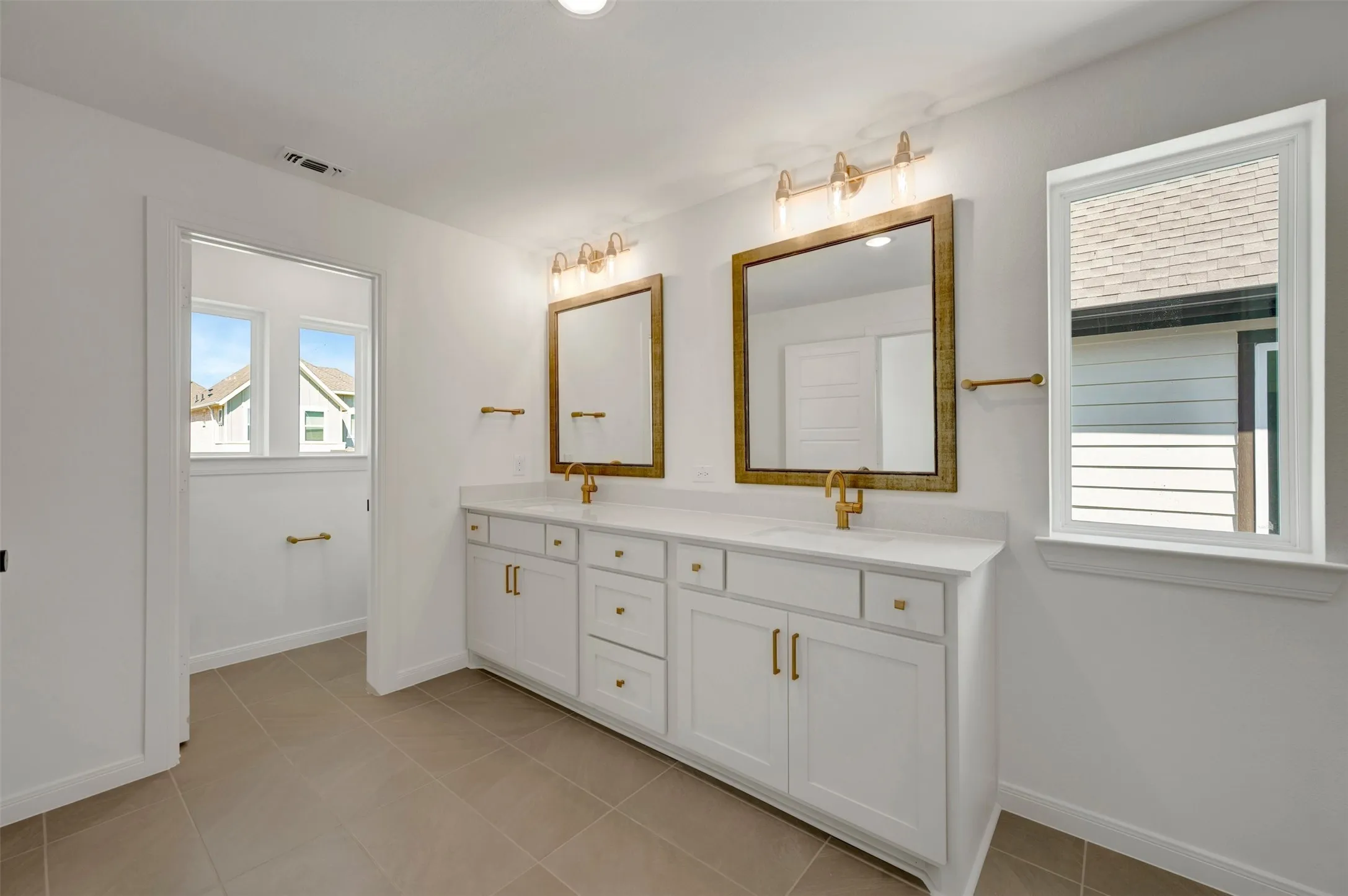 Dual vanity with white cabinetry, gold-finish hardware, individual mirrors, and built-in lighting