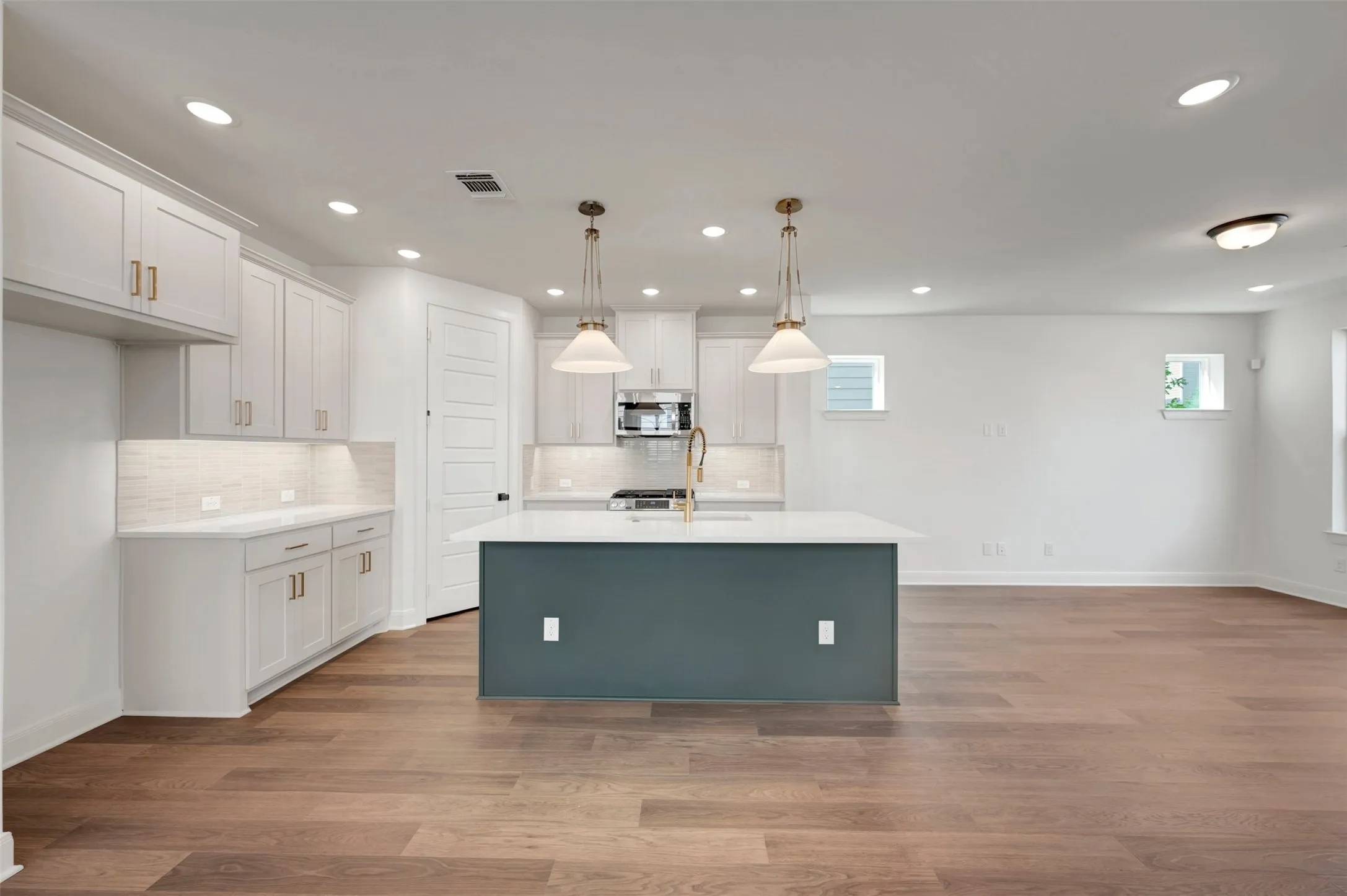 Kitchen and living area featuring wood-finish flooring, white cabinetry, a central island with a contrasting base, recessed lighting, and pendant lighting fixtures