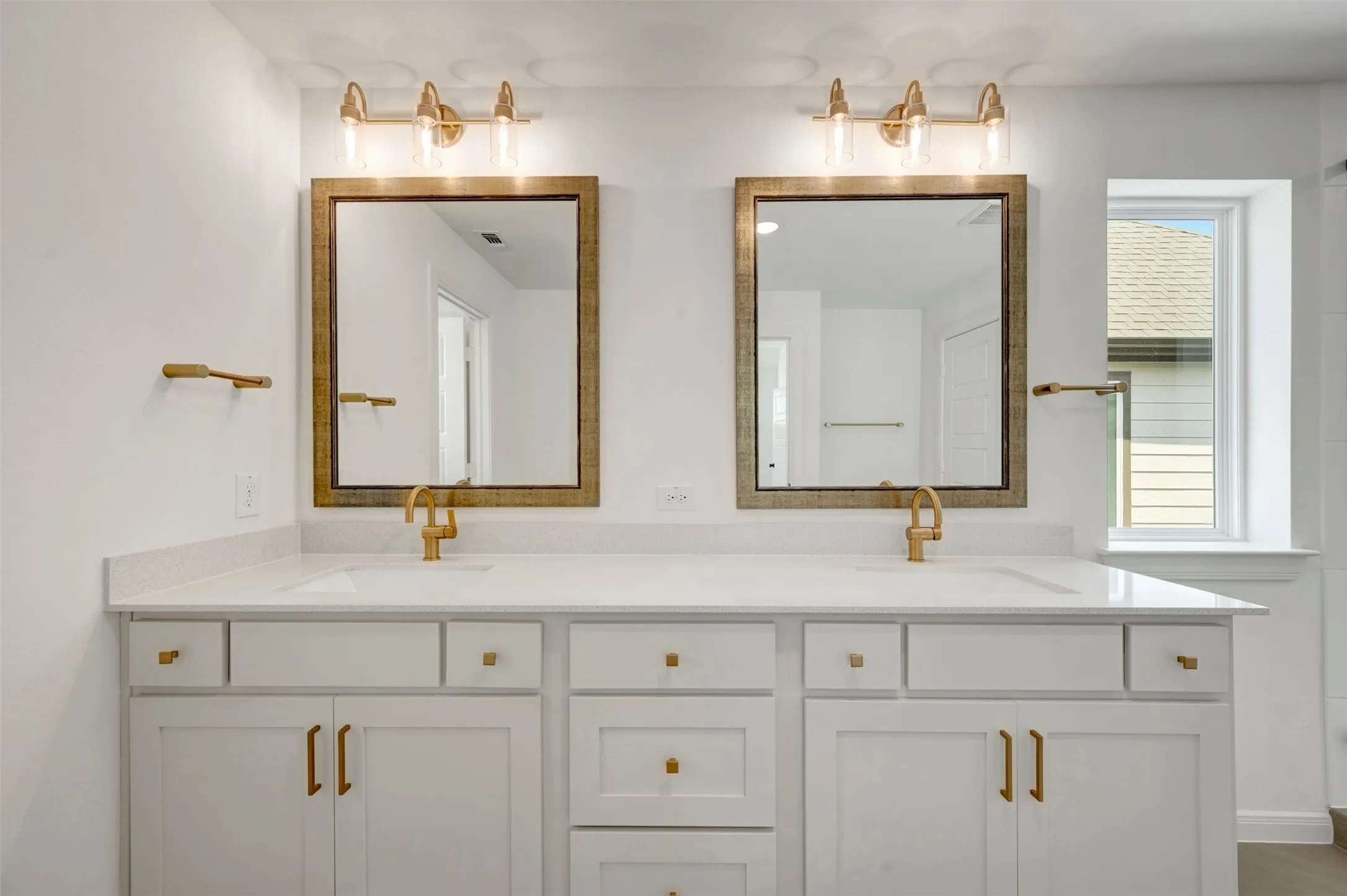 Dual vanity with white cabinetry, gold-finish hardware, and quartz countertops, illuminated by two three-light fixtures