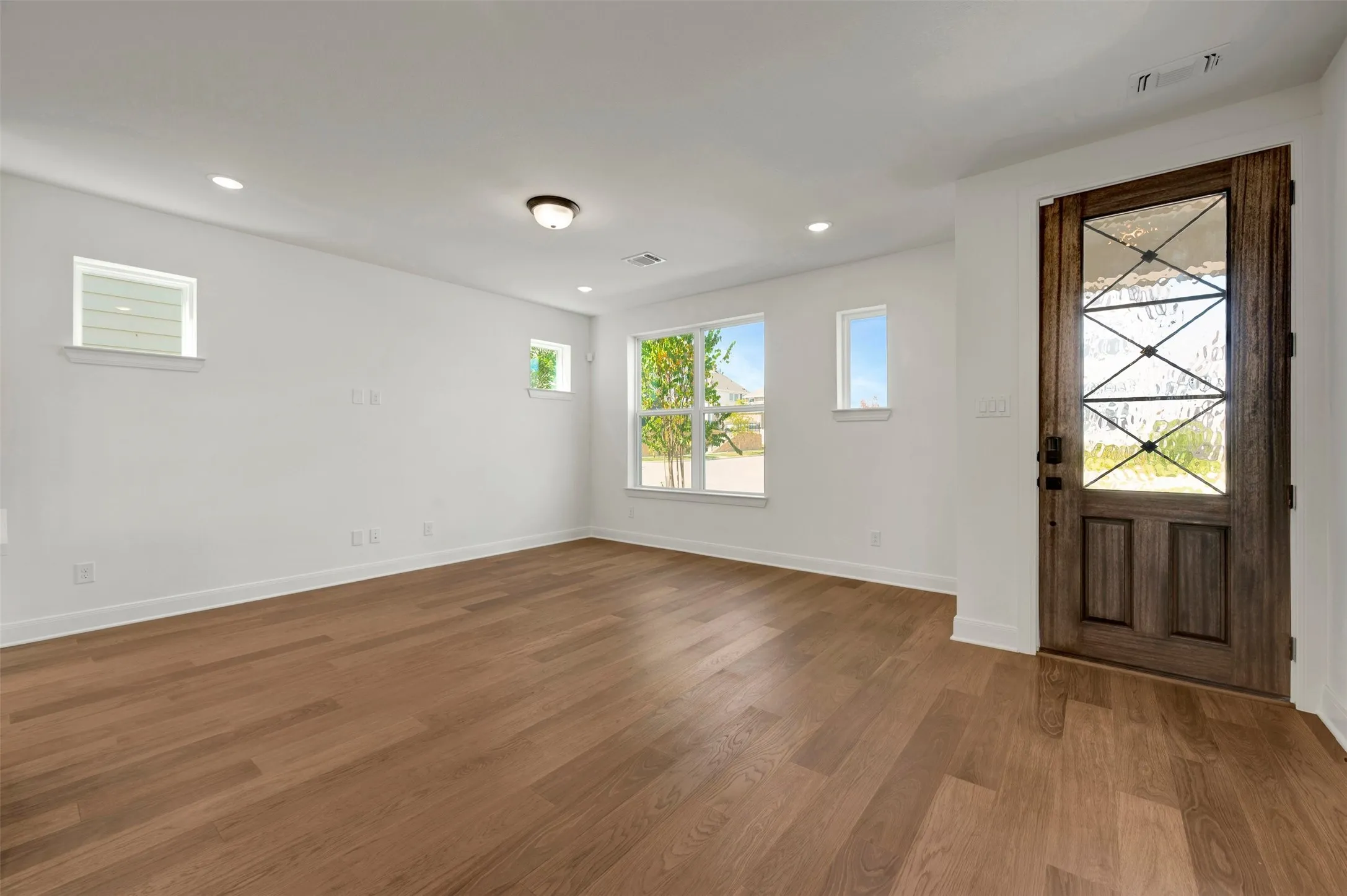 Wood-finish flooring, recessed lighting, and a prominent entry door with decorative glass