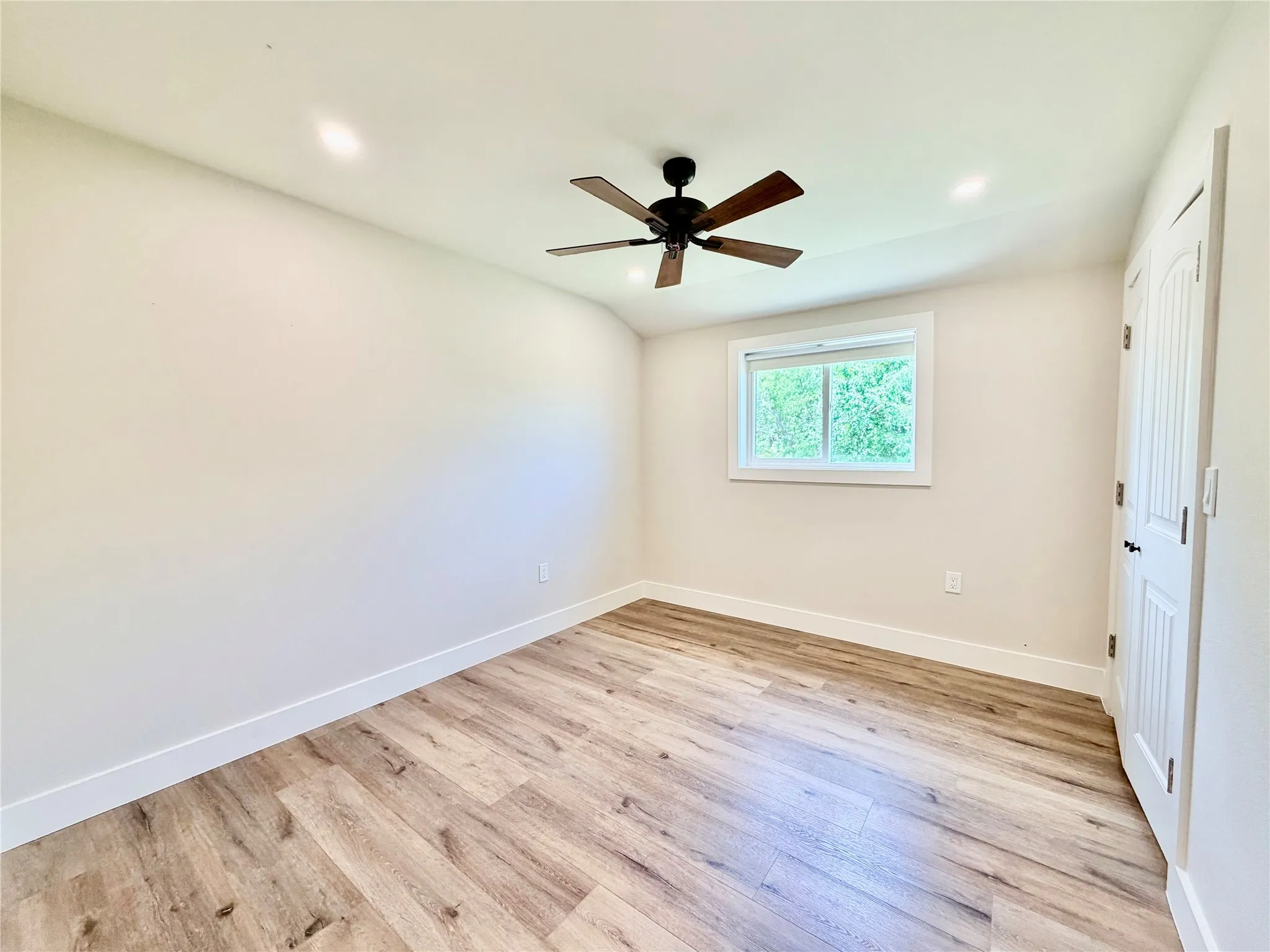 This spacious, light-filled bedroom serves as a peaceful retreat, showcasing clean lines, matching wood-look floors, and its own ceiling fan.