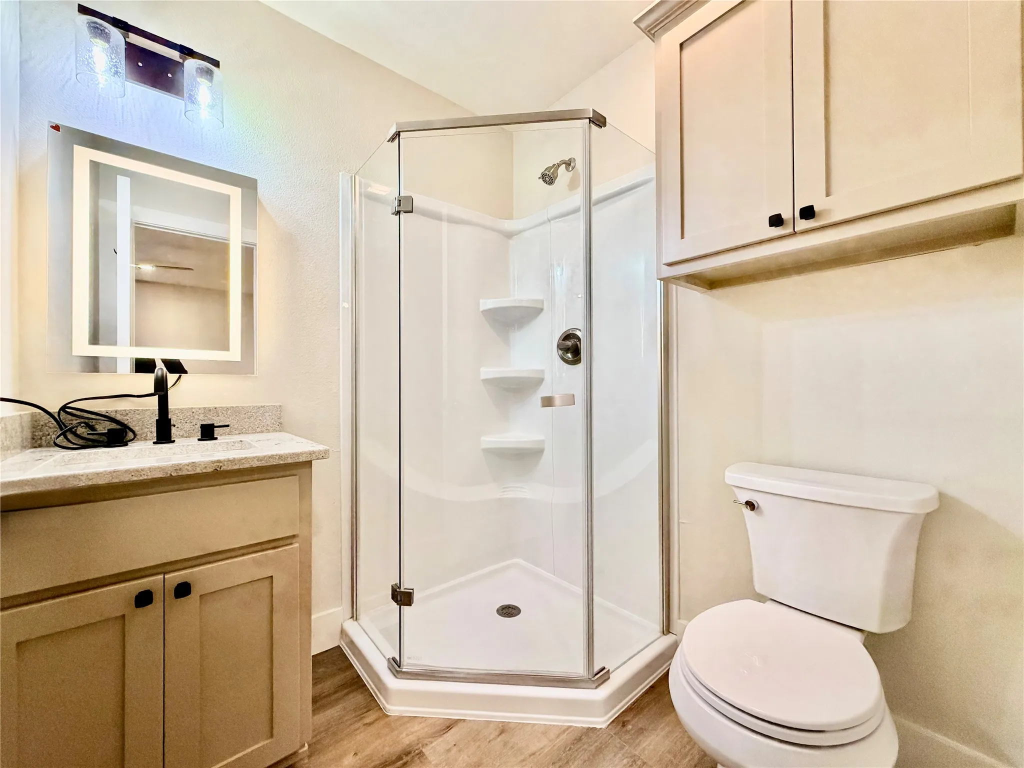Refresh in a pristine, modern bathroom equipped with a space-saving corner glass shower, stylish vanity, and excellent built-in storage cabinets.
