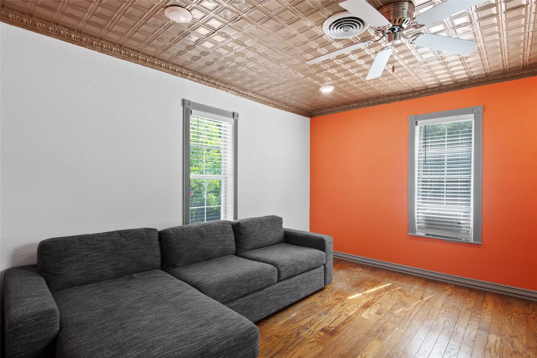 This room is a separate space upstairs, currently a living space and storage which features hardwood flooring, a unique patterned ceiling, and a ceiling fan for comfort.