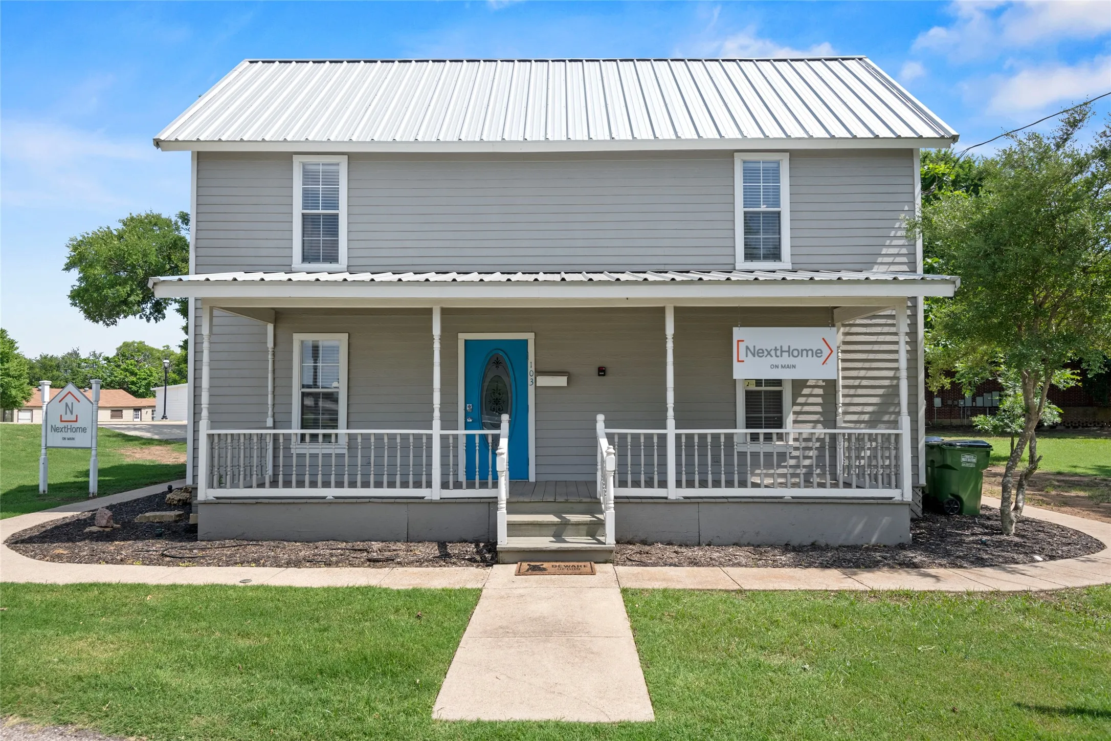 The property features a classic two-story facade with gray siding and a white metal roof.