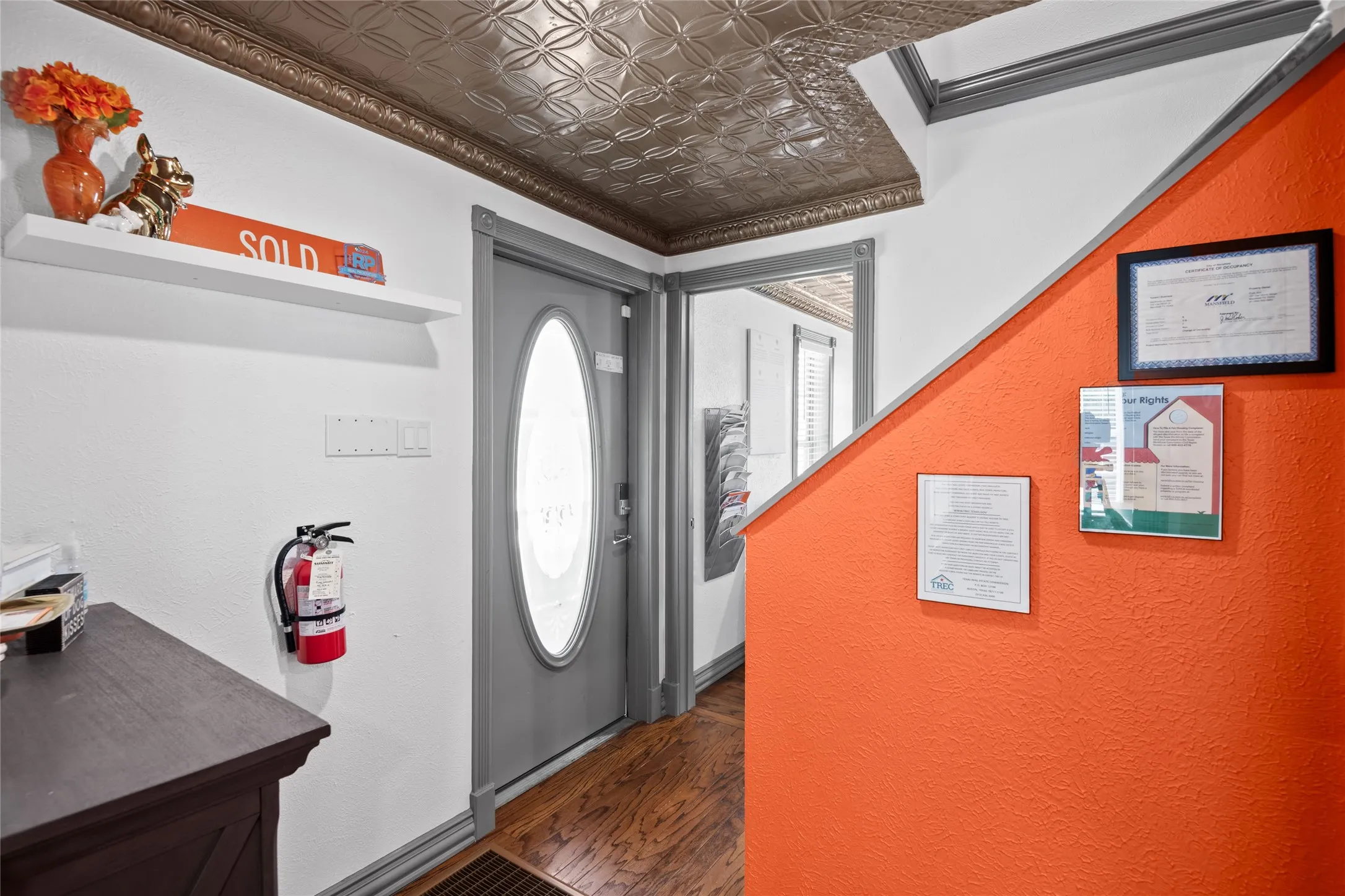 Entryway featuring hardwood flooring, a decorative tin ceiling, and a grey front door with an oval glass insert