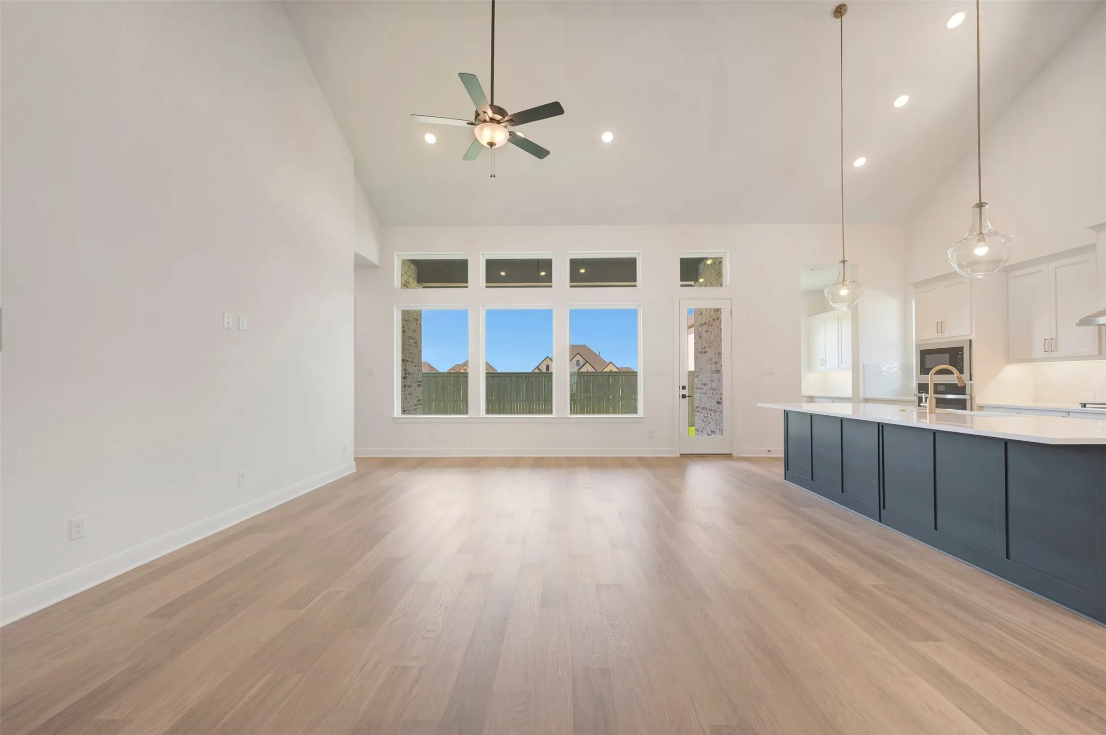 Vaulted ceiling, recessed lighting, wood-finish flooring, large windows, and a kitchen island with pendant lights