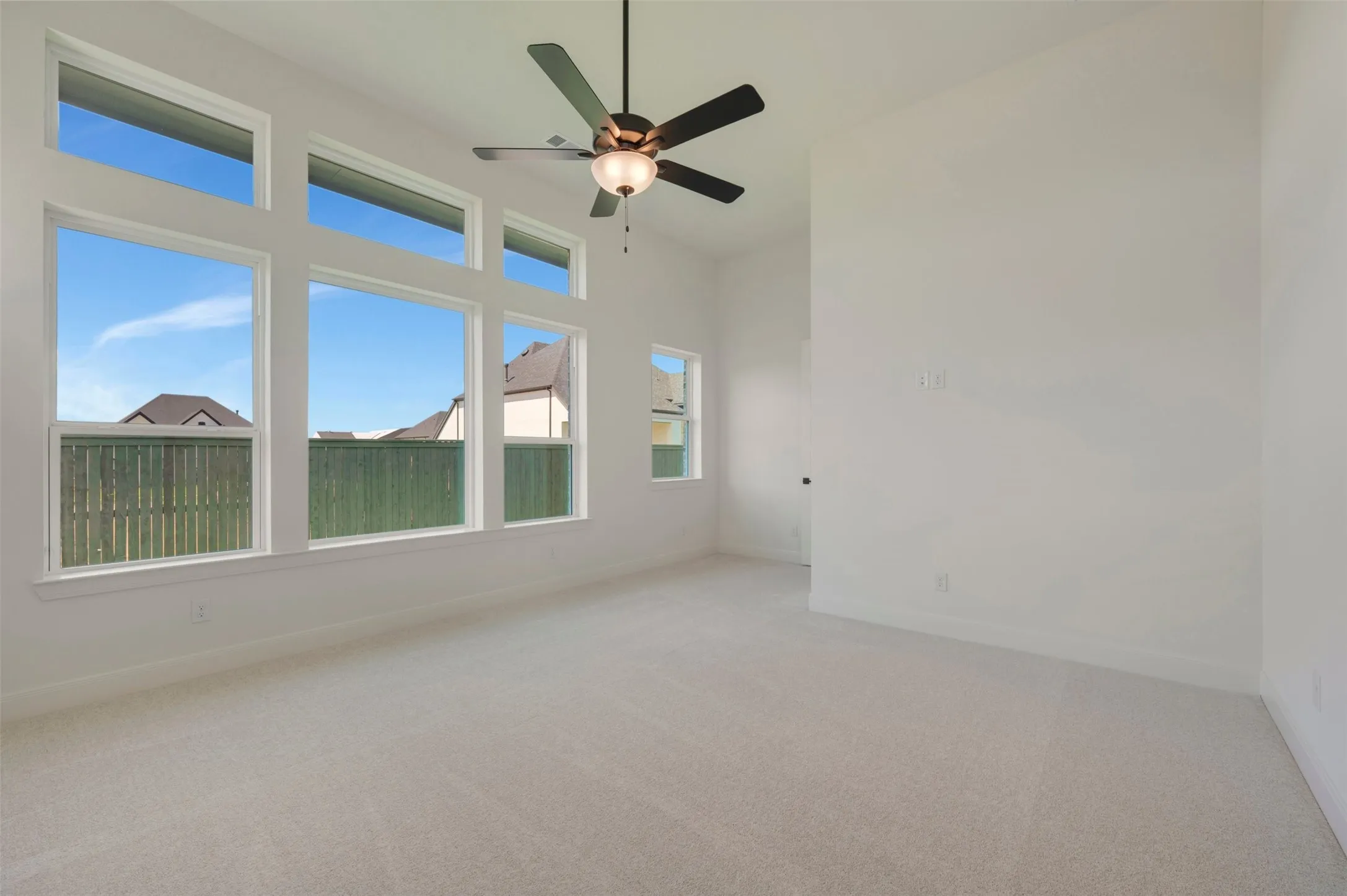 Expansive room with high ceilings, multiple large windows, a ceiling fan with integrated lighting, and neutral carpeting