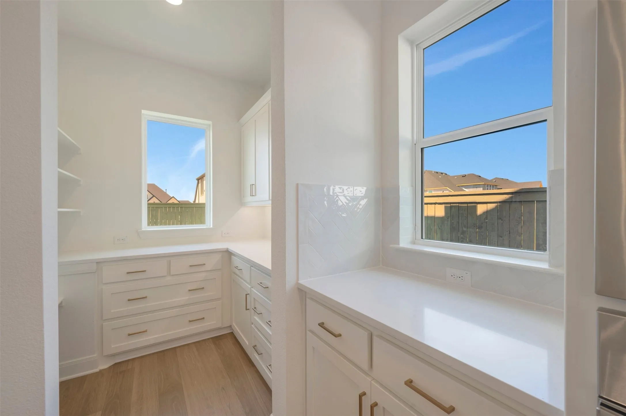 White cabinetry with gold-tone hardware, light-toned countertops, and wood-finish flooring