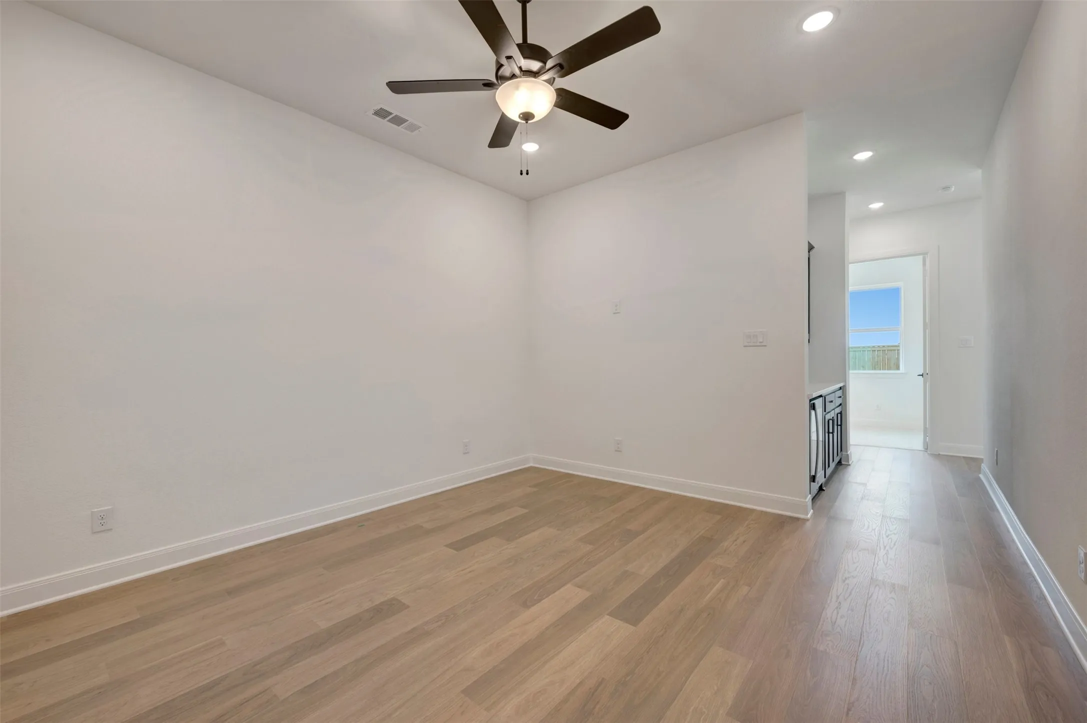 Spacious room featuring wood-finish flooring, recessed lighting, and a ceiling fan with integrated lighting