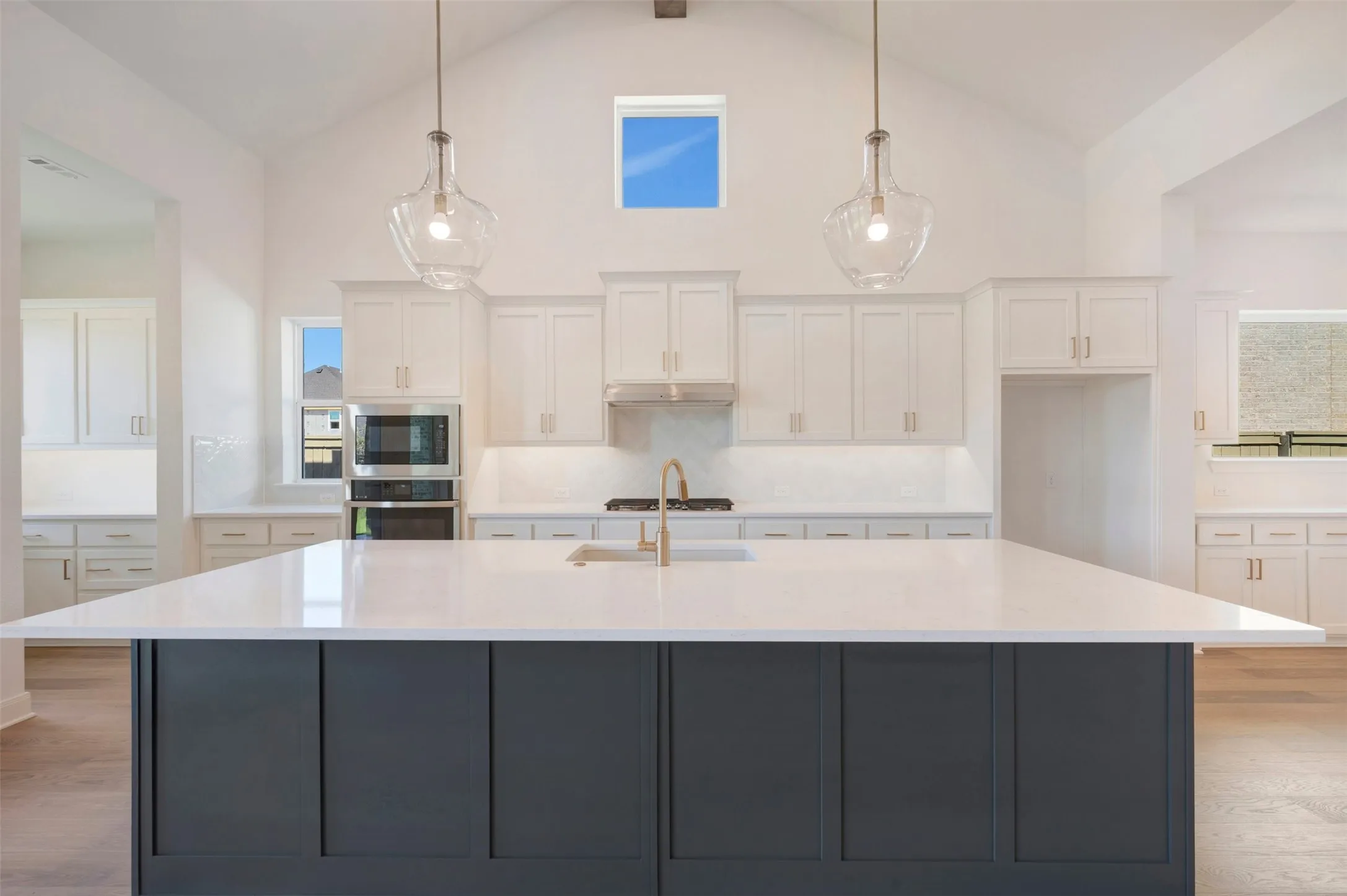 Kitchen featuring a large island with white countertop, white cabinetry, built-in stainless steel appliances, and vaulted ceilings