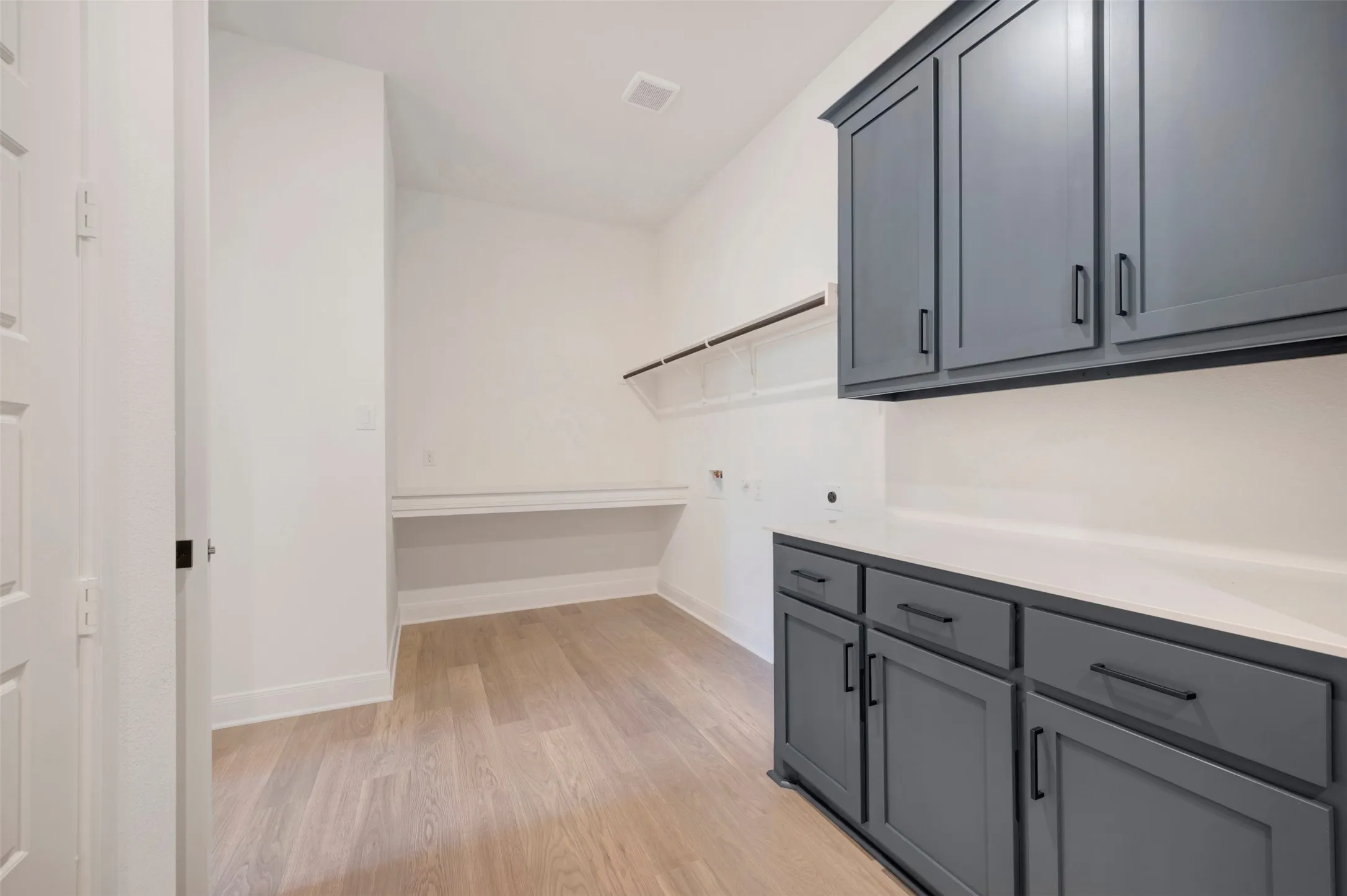 Light wood-finish flooring, built-in shelving, white countertops, and dark gray cabinetry with black hardware