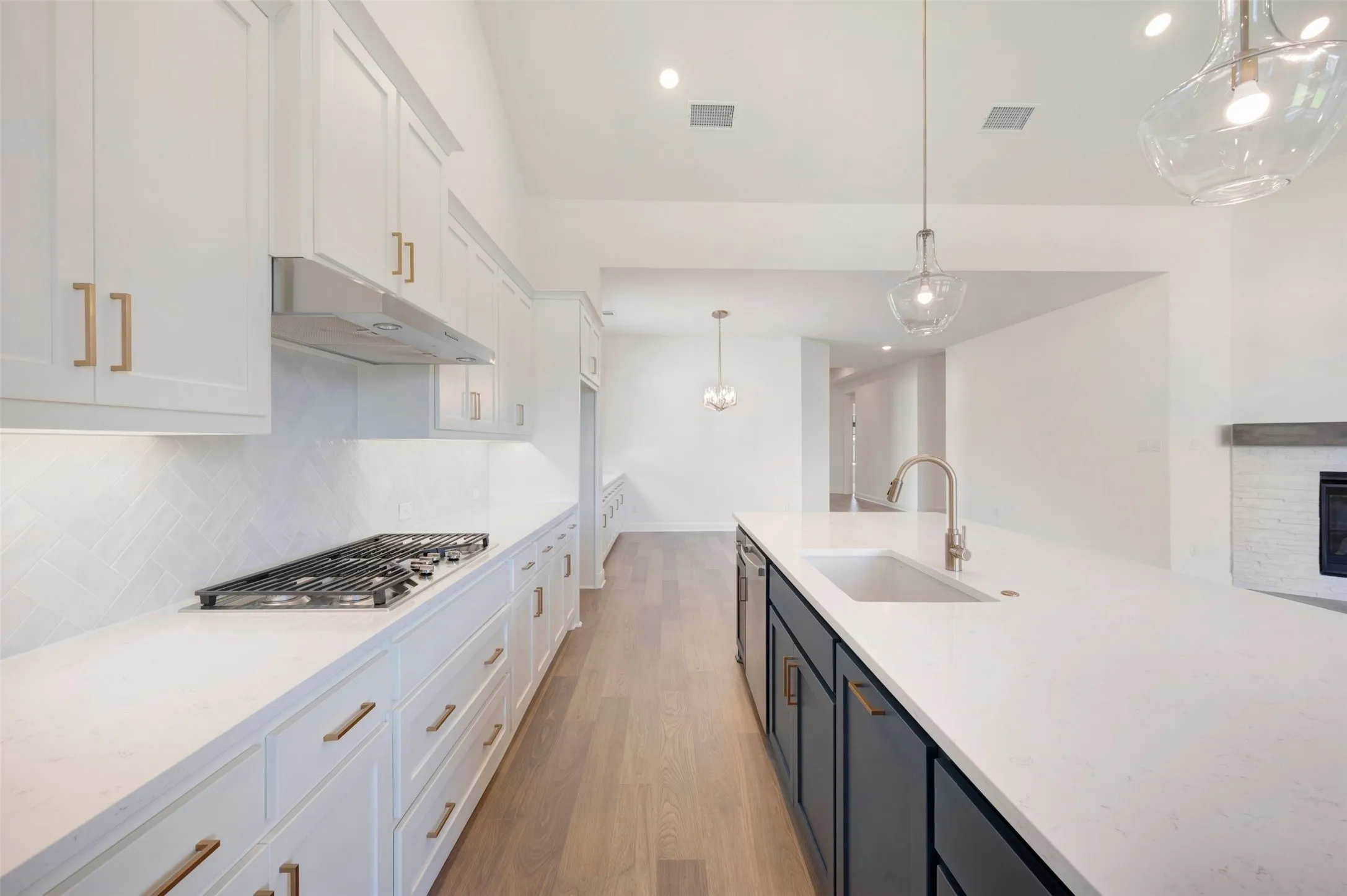 Kitchen featuring white shaker-style cabinetry, white countertops, a gas cooktop, a large kitchen island with an undermount sink, and wood-finish flooring