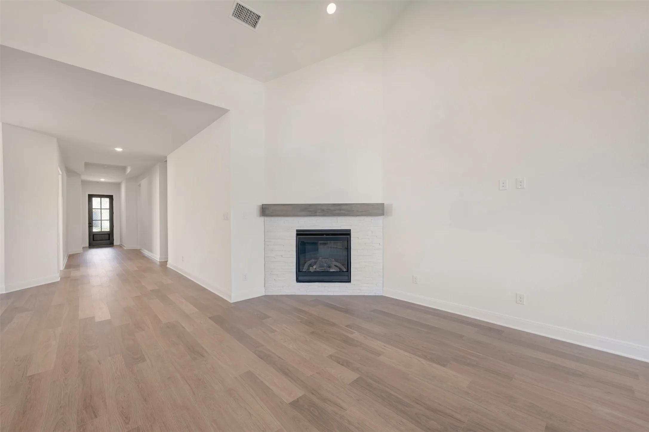 Vaulted ceilings with recessed lighting, corner fireplace featuring a white brick surround and wood-finish mantel, and light wood-finish flooring