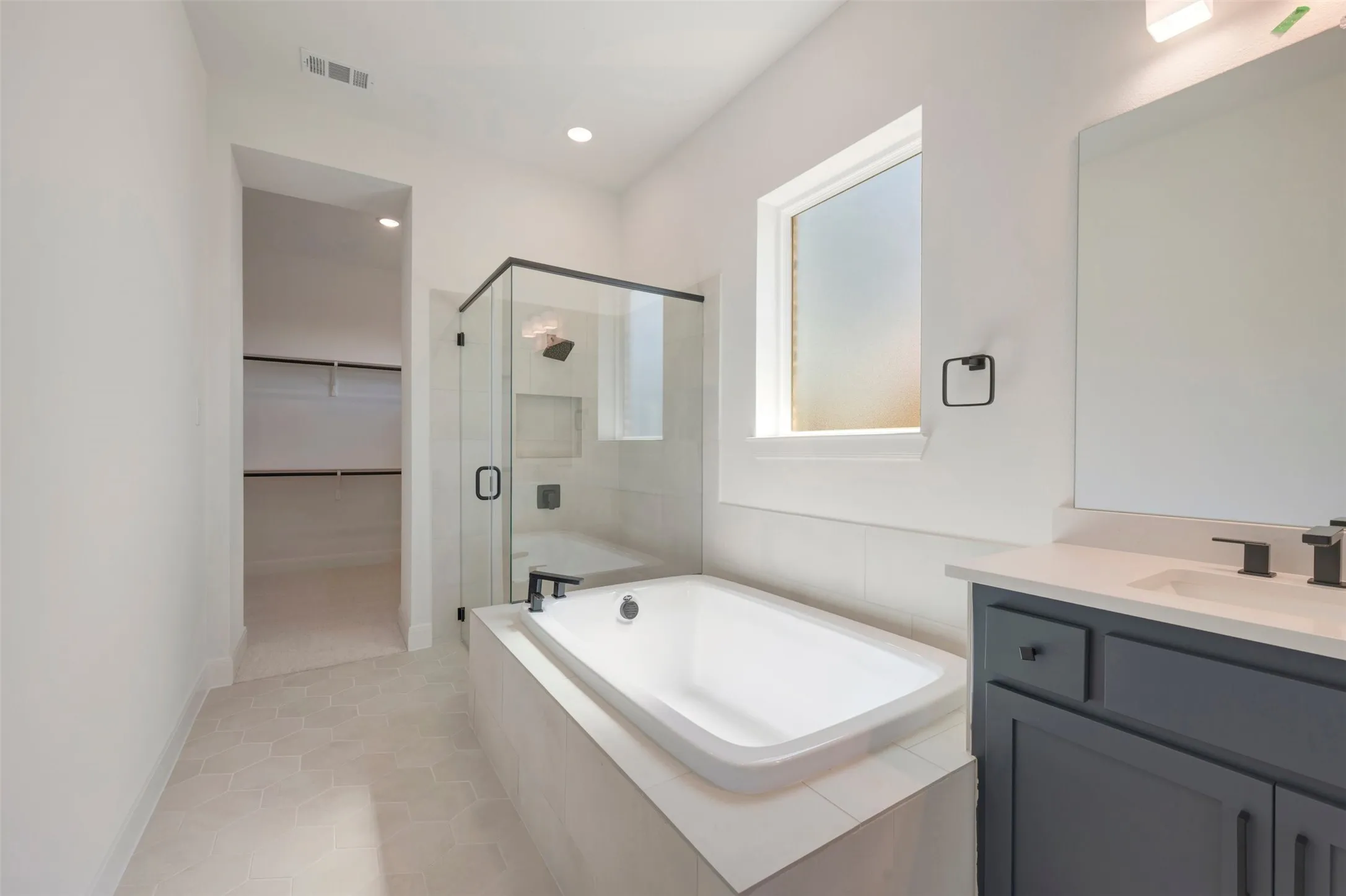 Freestanding bathtub with surrounding tile, glass-enclosed shower, vanity with integrated sink and storage, and a walk-in closet with built-in shelving