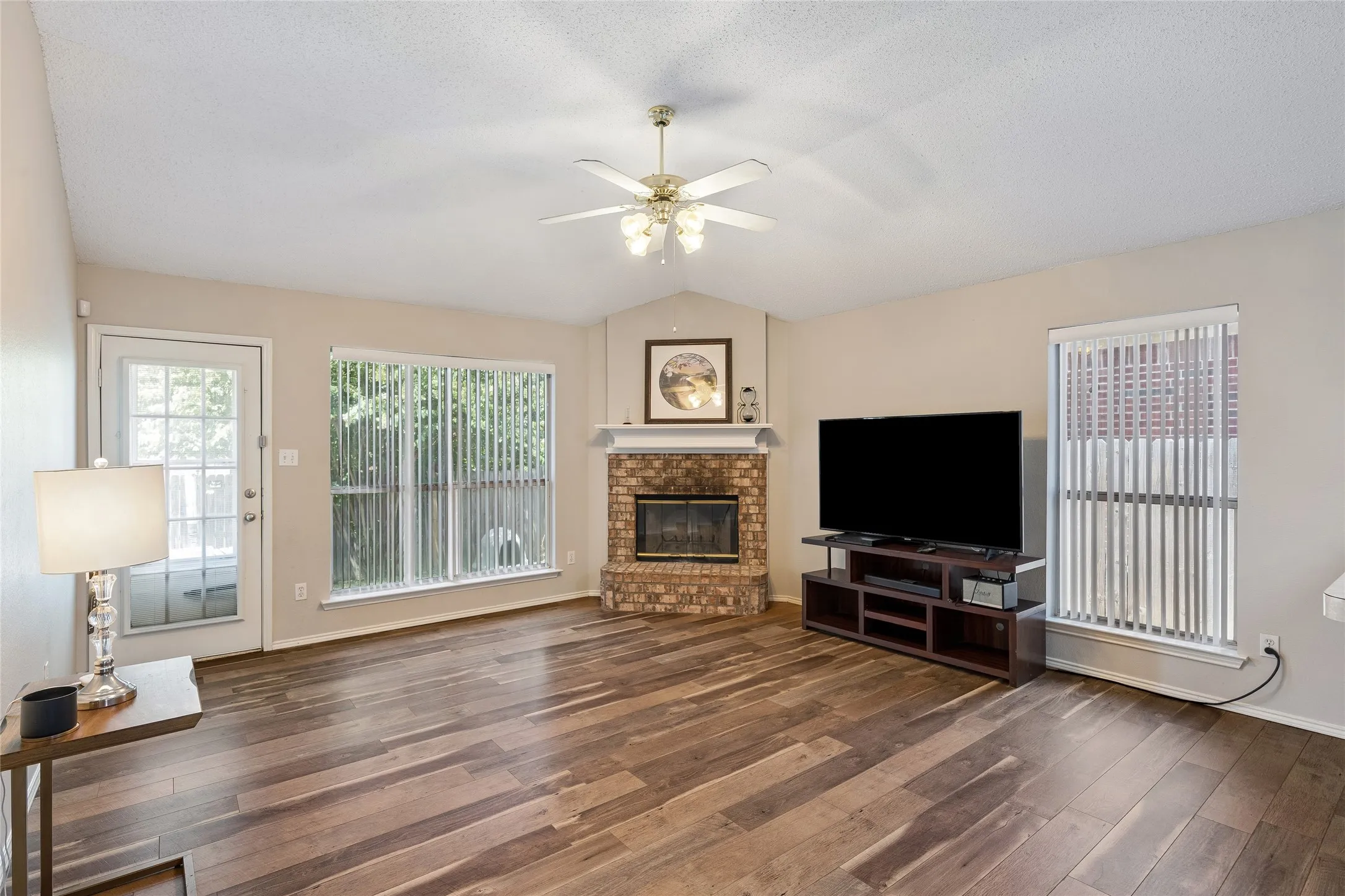 The cozy den features a brick fireplace & engineered-wood plank flooring.