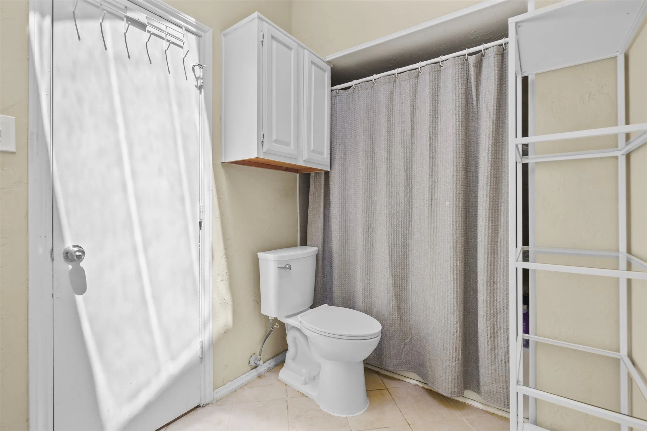 Bathroom featuring a white toilet, tiled flooring, and a shower area with a curtain