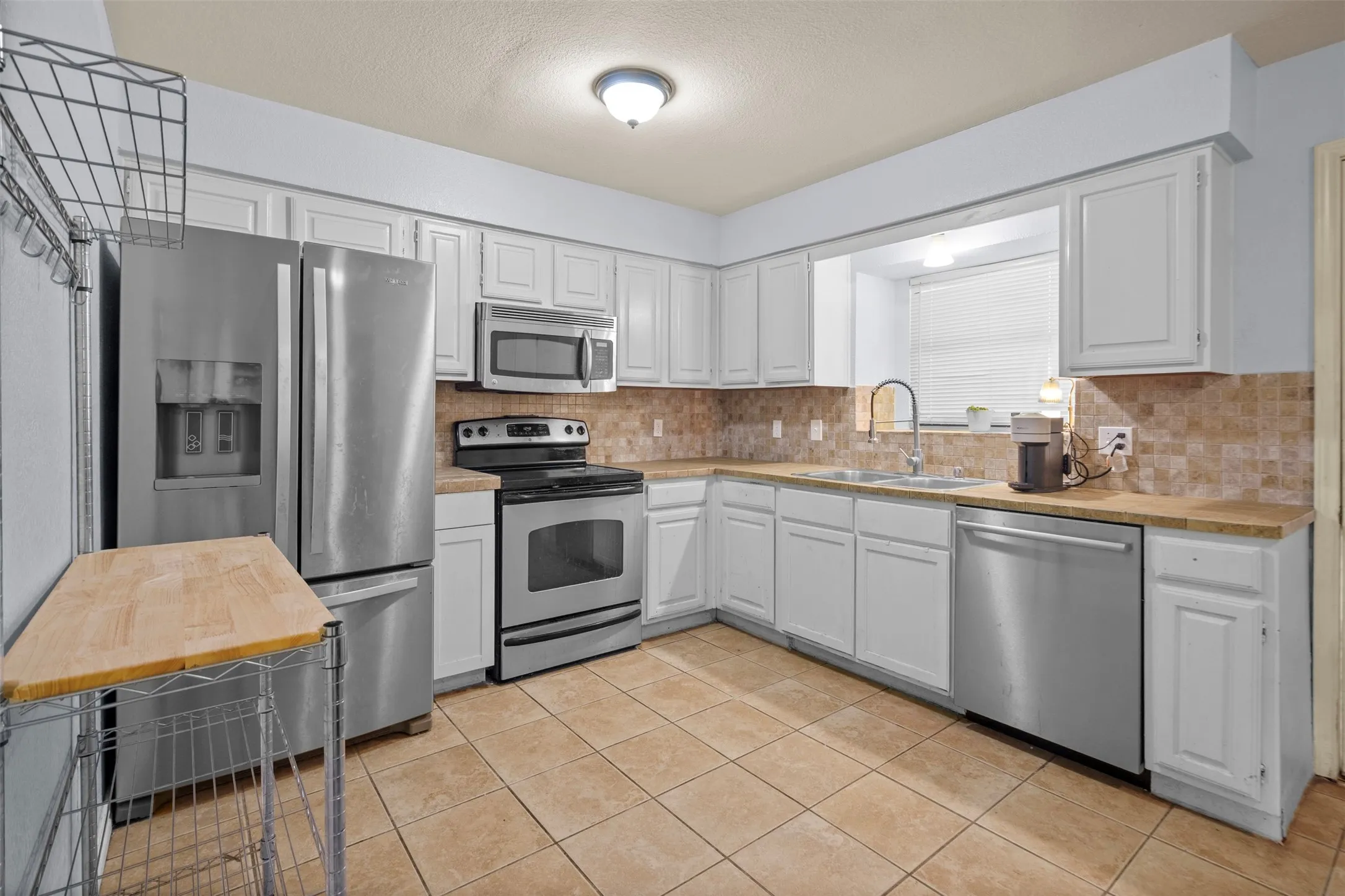 Kitchen featuring white cabinetry, stainless steel appliances, tiled backsplash, light-toned countertops, and ceramic tile flooring