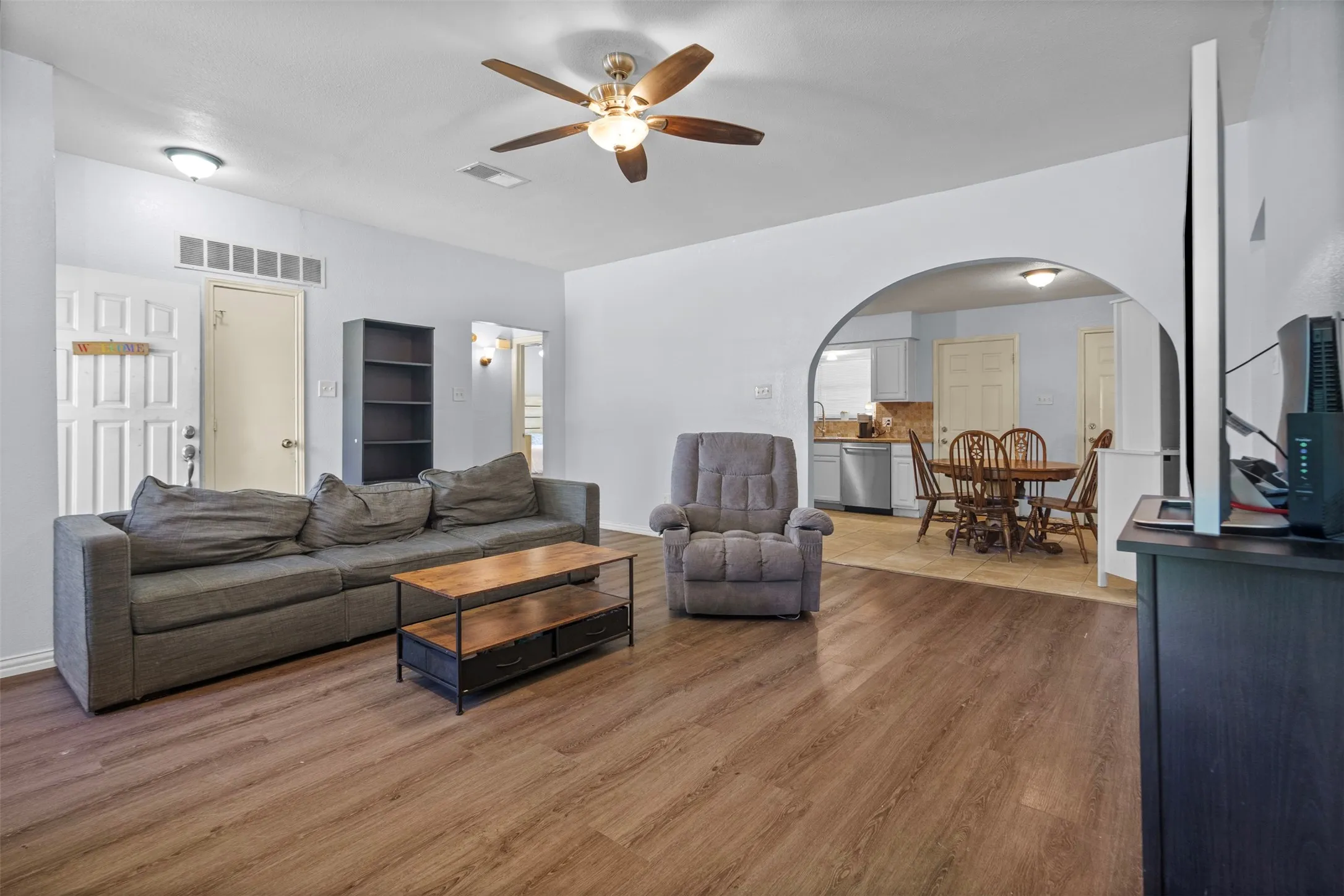 Open-concept living area with wood-finish flooring, an arched doorway, and an overhead ceiling fan with lighting