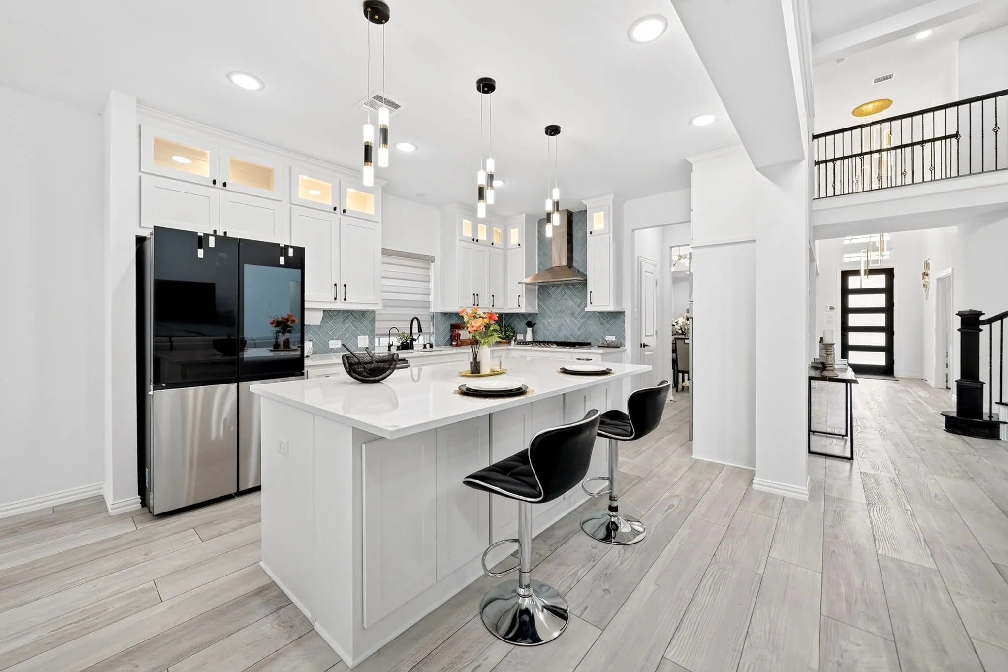 Modern kitchen featuring a large central island with seating, stainless steel appliances, white cabinetry with display lighting, a patterned tile backsplash, and light wood-finish flooring
