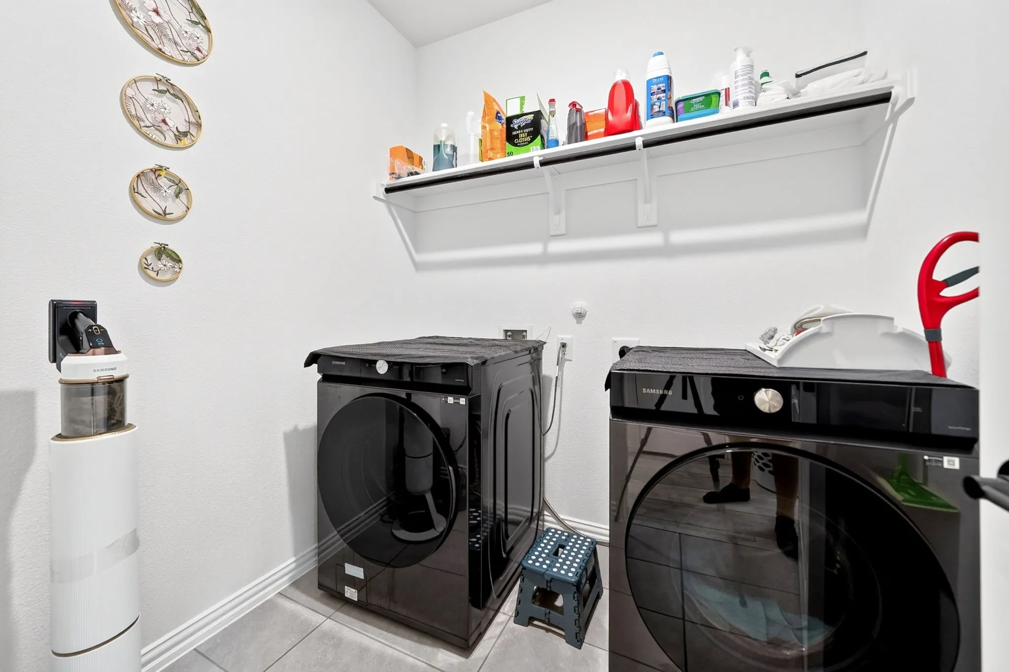 Dedicated laundry space featuring a white wall-mounted storage shelf, light-toned floor tile, and crisp white baseboards