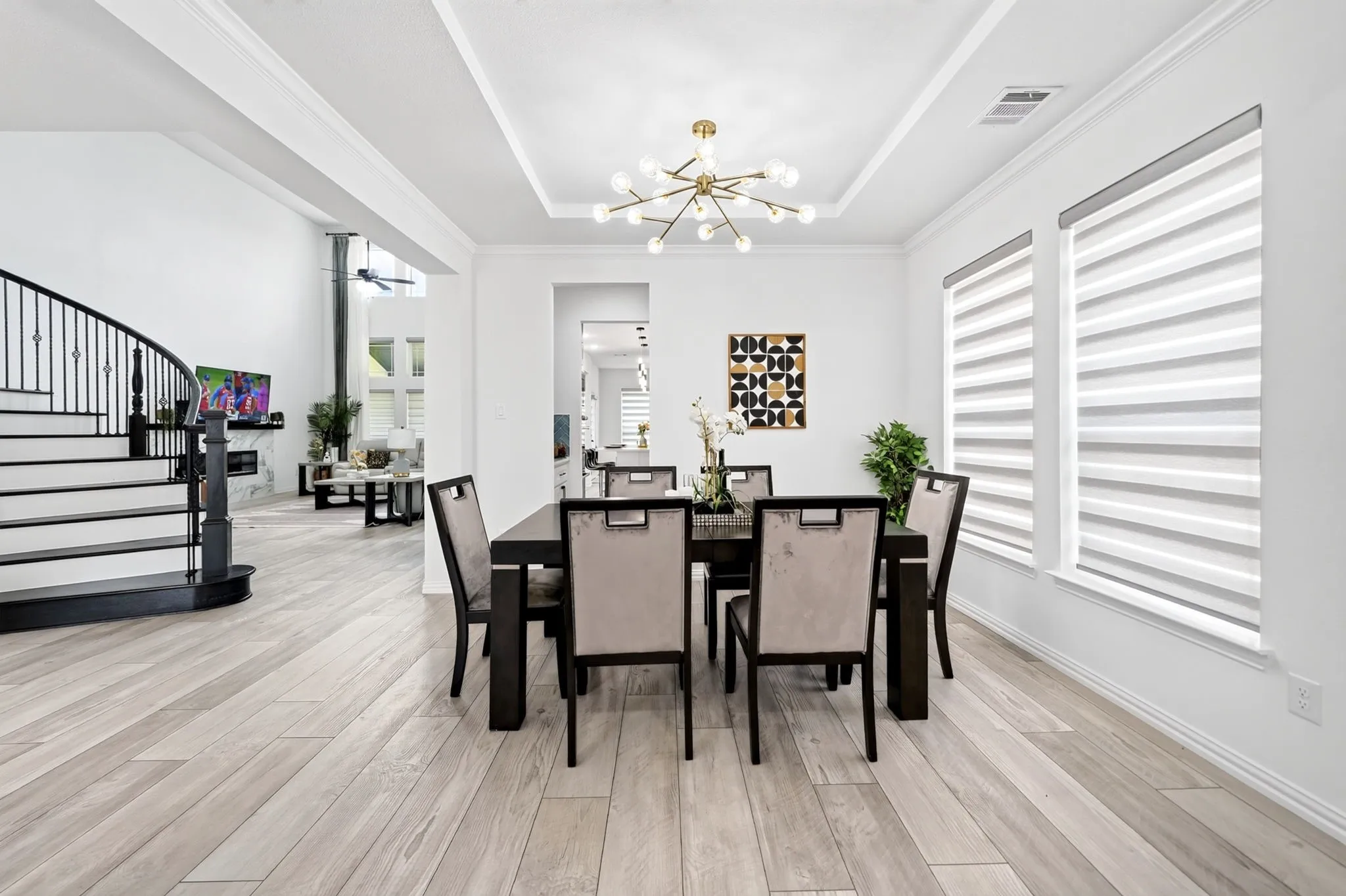 Formal dining space featuring a modern chandelier, tray ceiling, and dual windows with layered shades