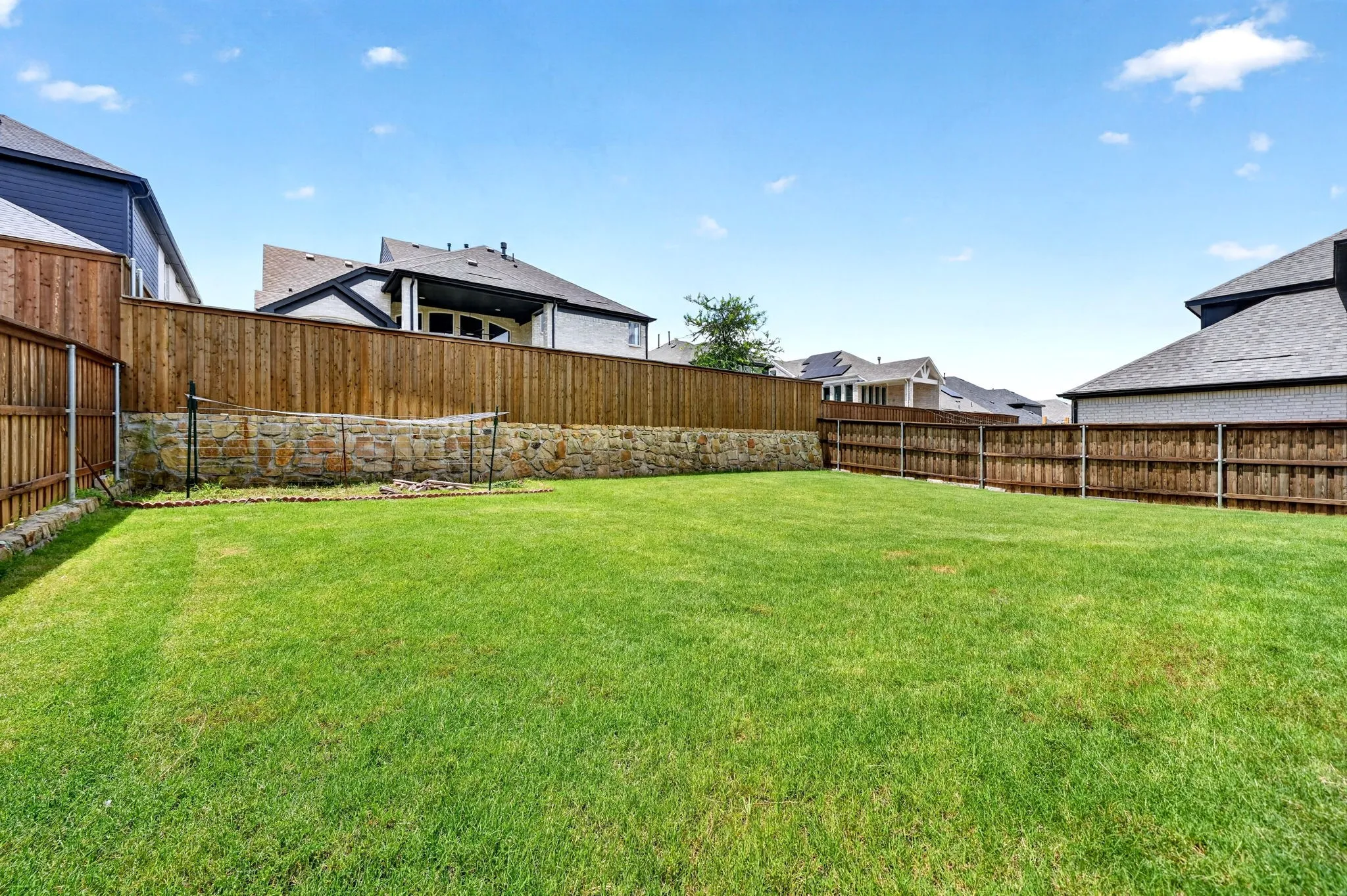 Expansive rear yard featuring a large grass lawn, perimeter wood fencing, and a stone retaining wall