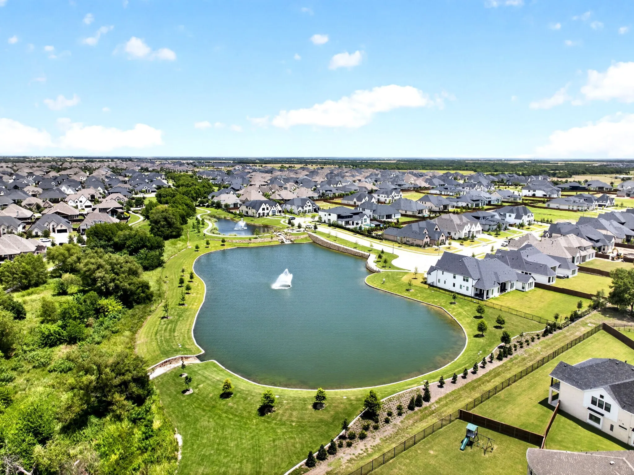 Expansive residential community featuring a prominent central lake with fountain, surrounded by manicured green spaces and paved pathways