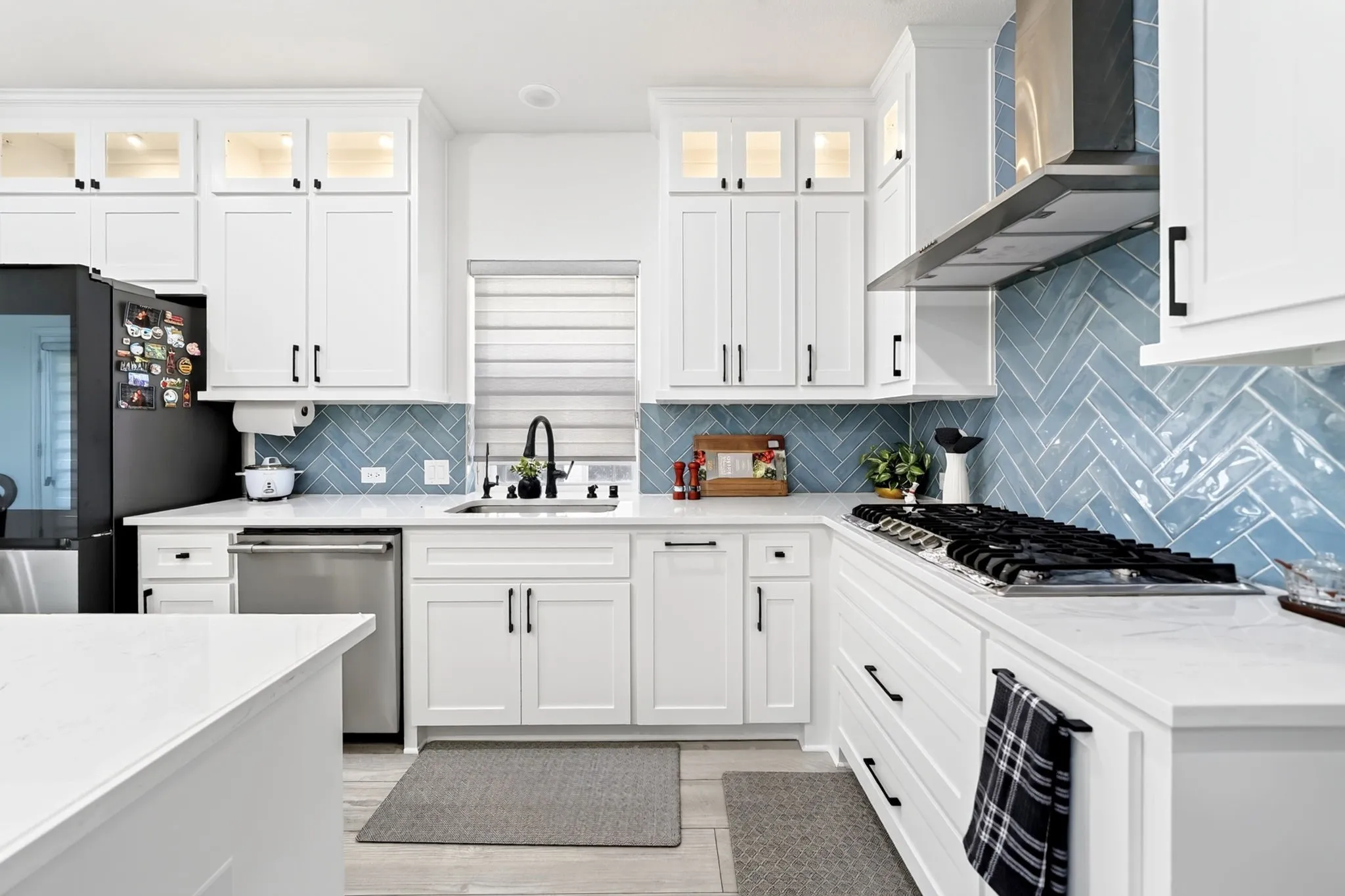 Contemporary kitchen featuring white shaker cabinetry, light countertops, and a blue herringbone tile backsplash