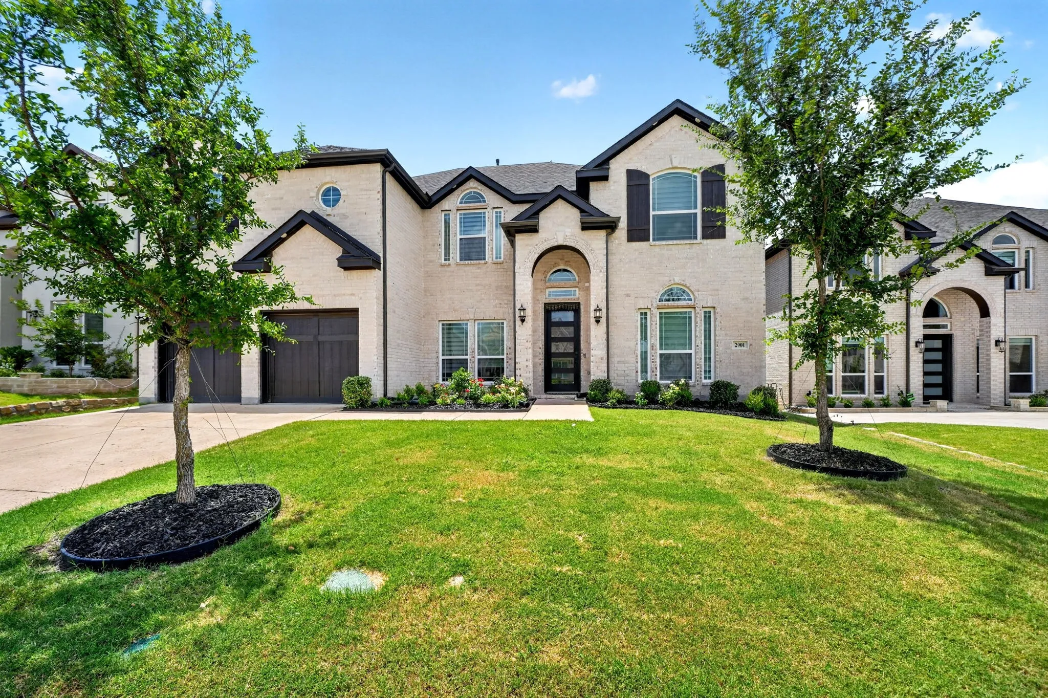 Two-story brick exterior featuring dark trim accents, a two-car garage, and an arched entryway