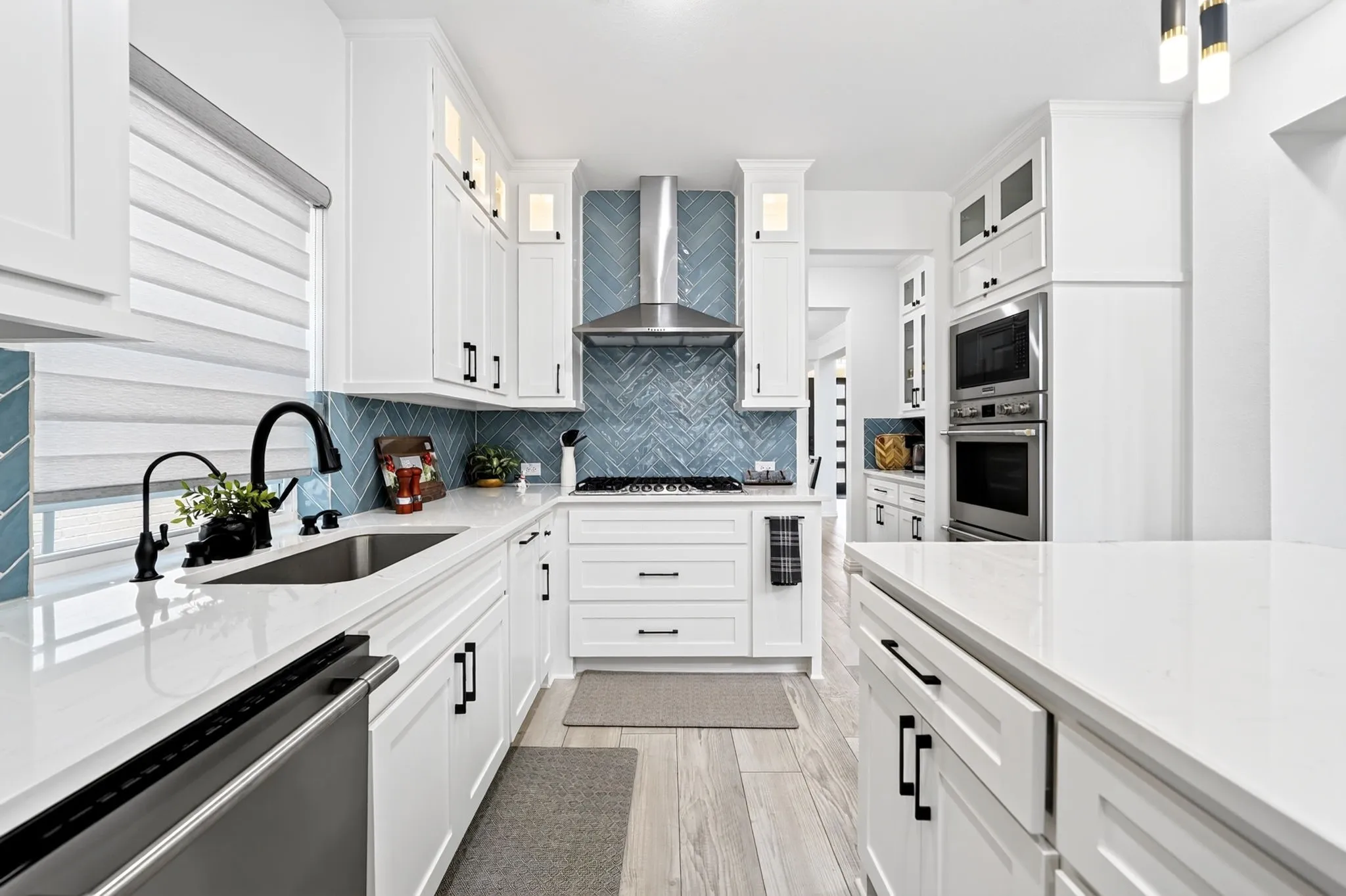 Modern kitchen featuring white shaker cabinetry, white countertops, stainless steel appliances, a blue herringbone tile backsplash, and light wood-finish flooring