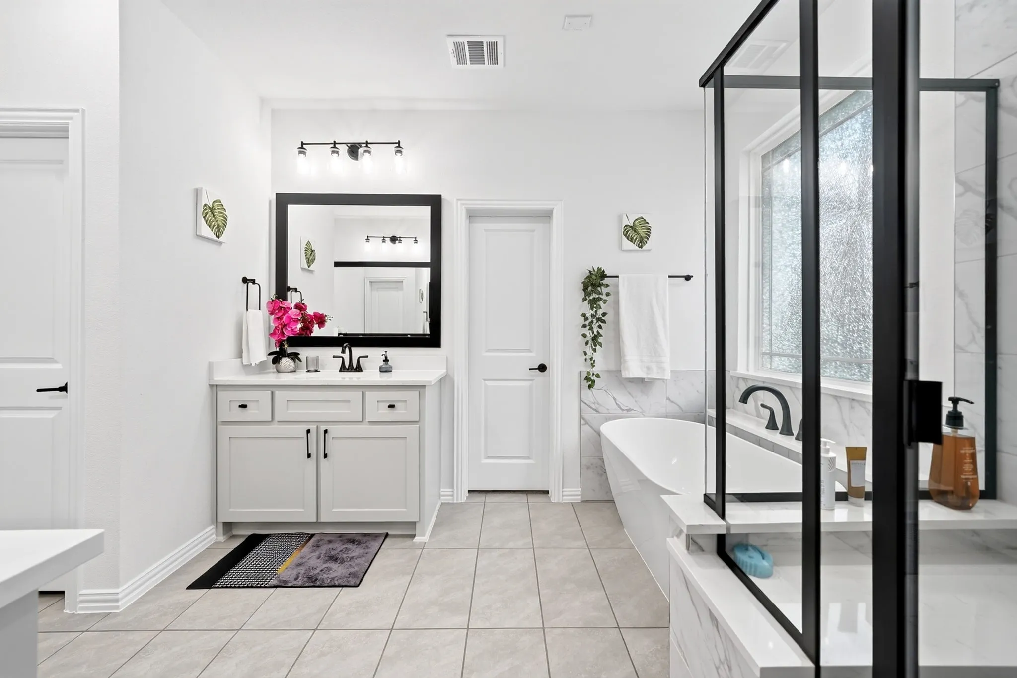 Contemporary bathroom featuring a freestanding tub, a glass-enclosed shower with black framing, a single vanity with a white countertop, and tiled flooring