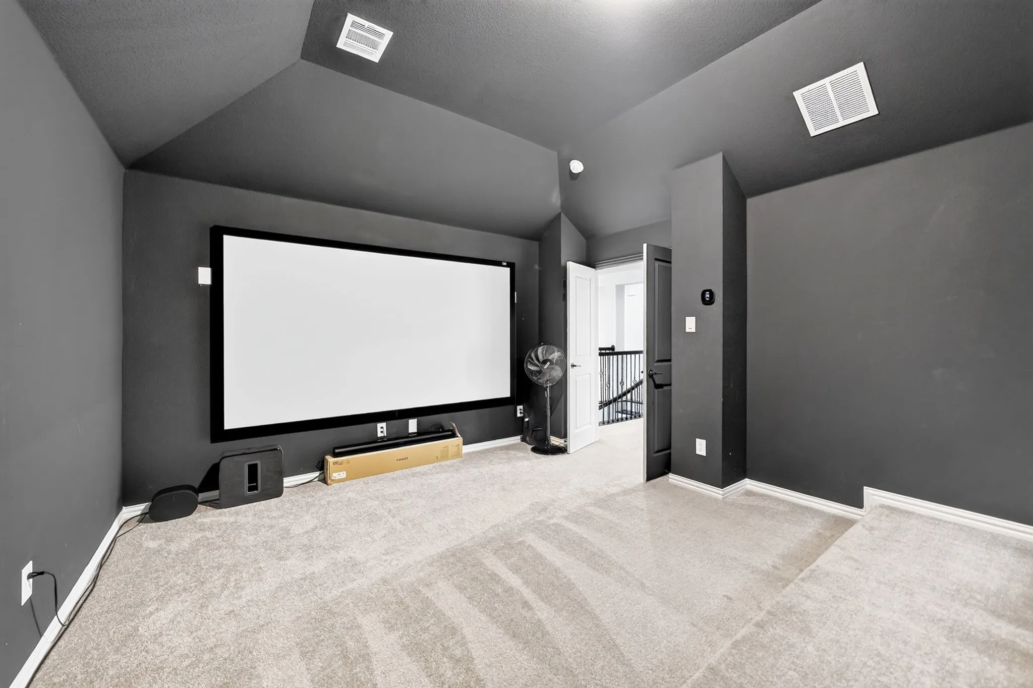 Dedicated media room featuring a large projection screen, dark wall finishes, sloped ceiling, recessed lighting, and light-toned carpet flooring