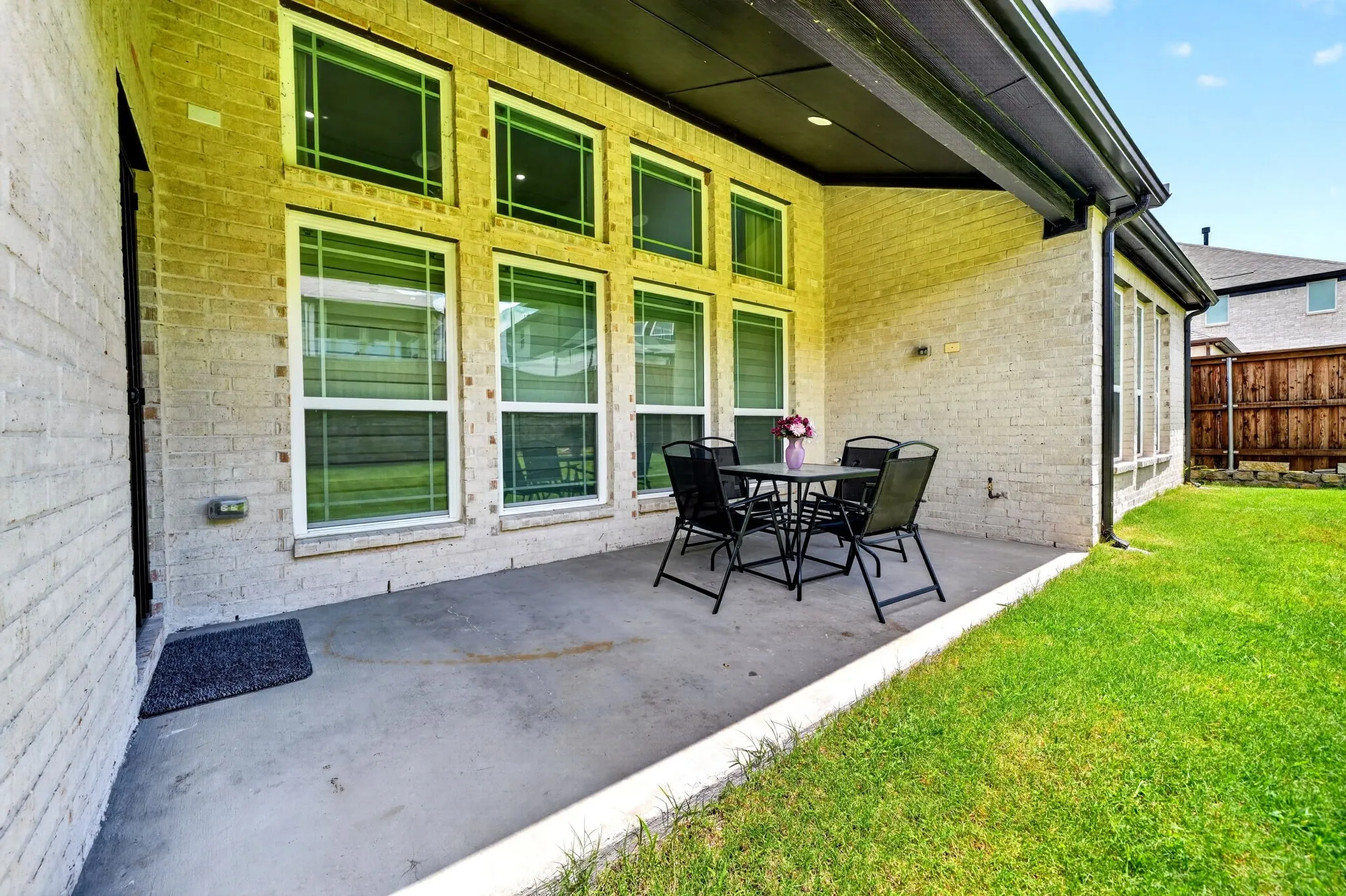 Covered concrete patio with a brick exterior, multiple windows, and a manicured lawn