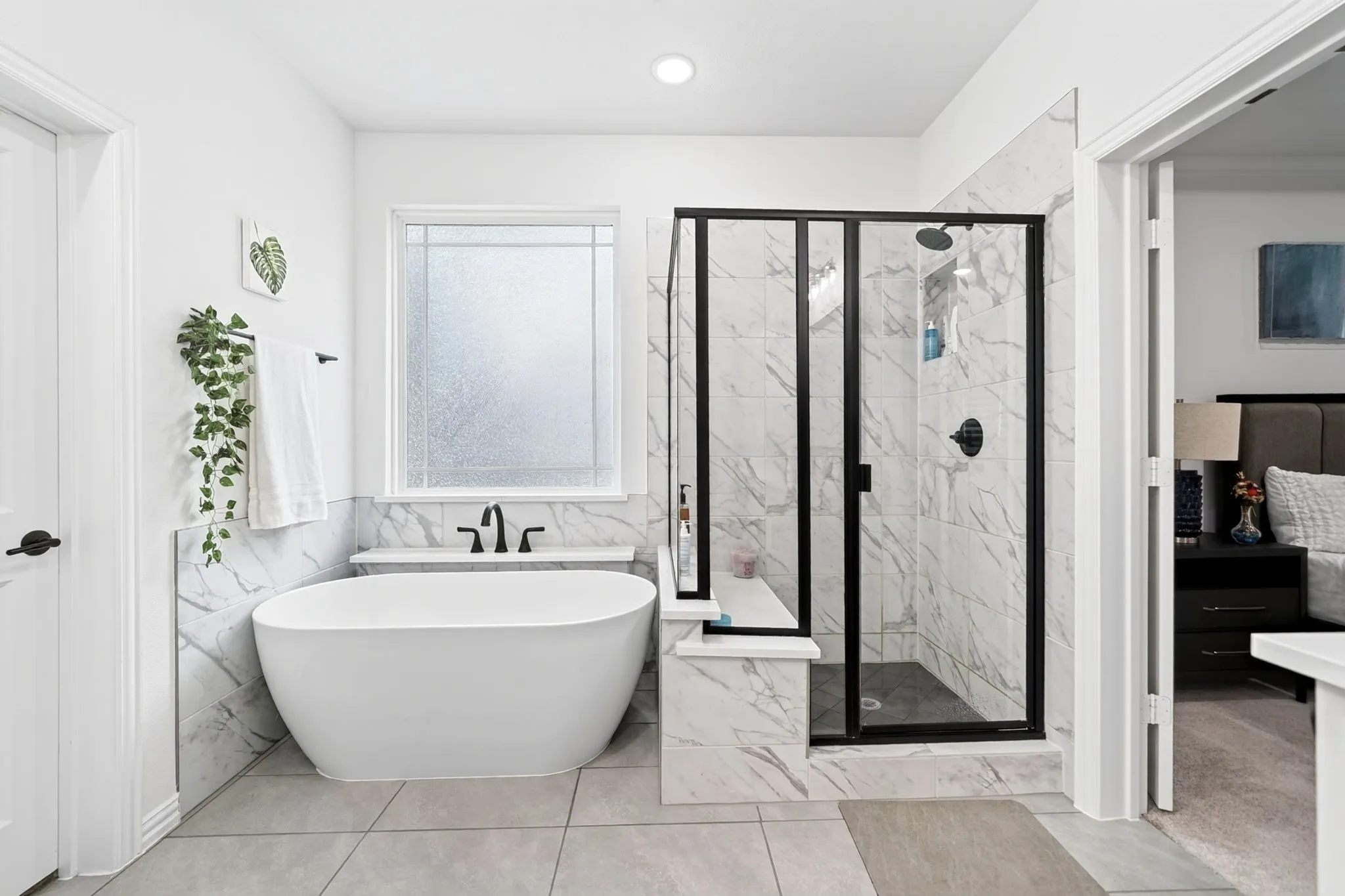 Bathroom featuring a freestanding soaking tub with matte black fixtures, a frosted privacy window, and a glass-enclosed shower with matte black trim and stone-look tile surround