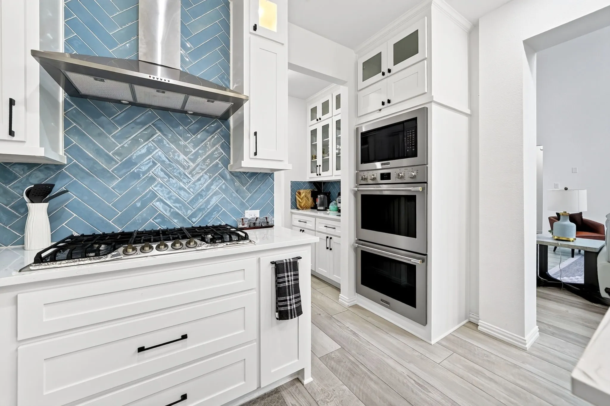 Kitchen featuring a herringbone tile backsplash, stainless steel range hood, built-in gas cooktop, white shaker cabinetry, and built-in stainless steel double ovens