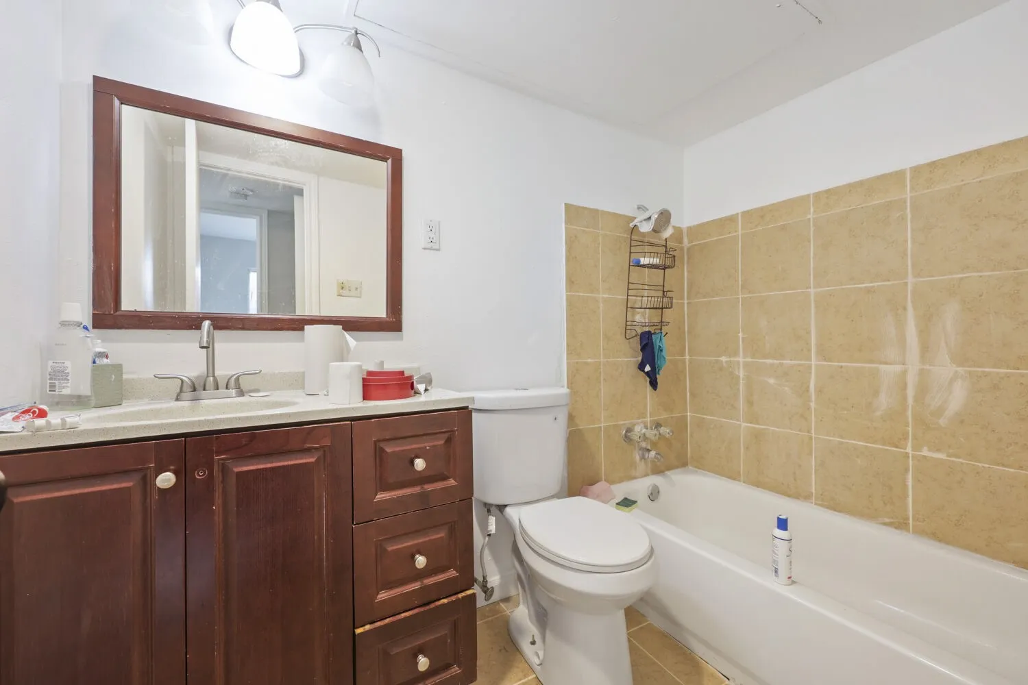 Bathroom featuring a wood-finish vanity with an integrated sink, a framed mirror, a standard toilet, and a bathtub with tiled surround
