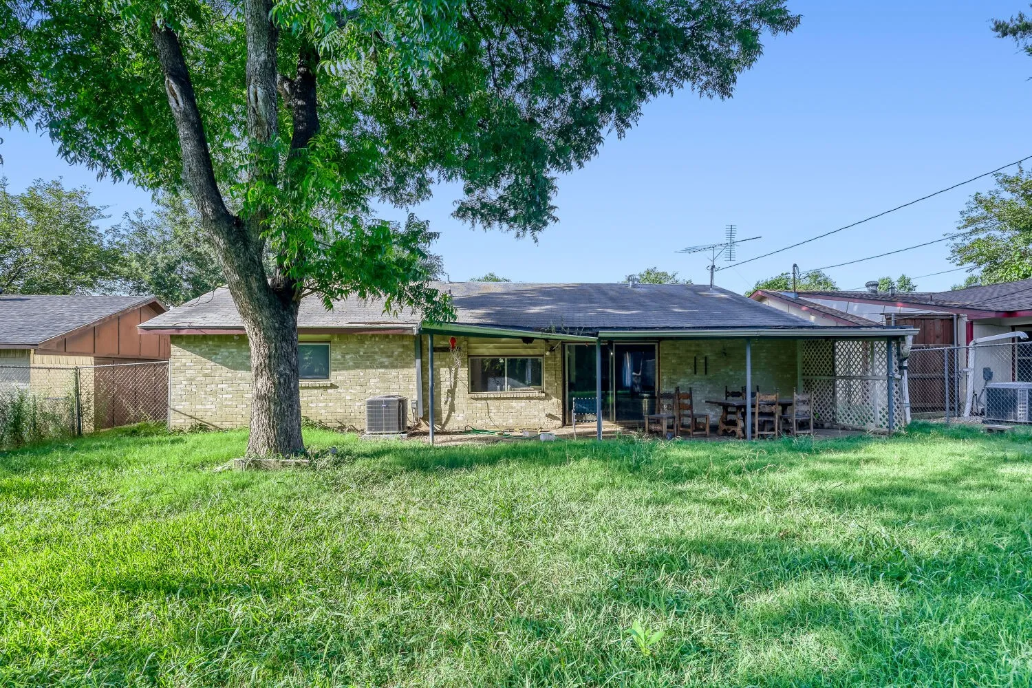 Spacious rear yard with a mature shade tree, brick exterior, covered patio, and privacy fencing