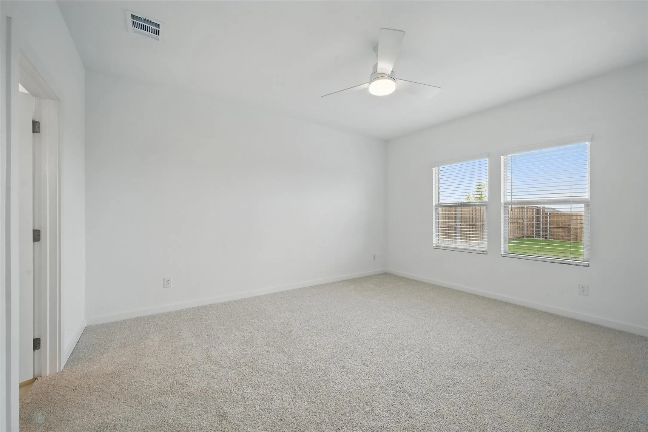 Carpeted room featuring a ceiling fan with integrated lighting, two windows with blinds, and white walls