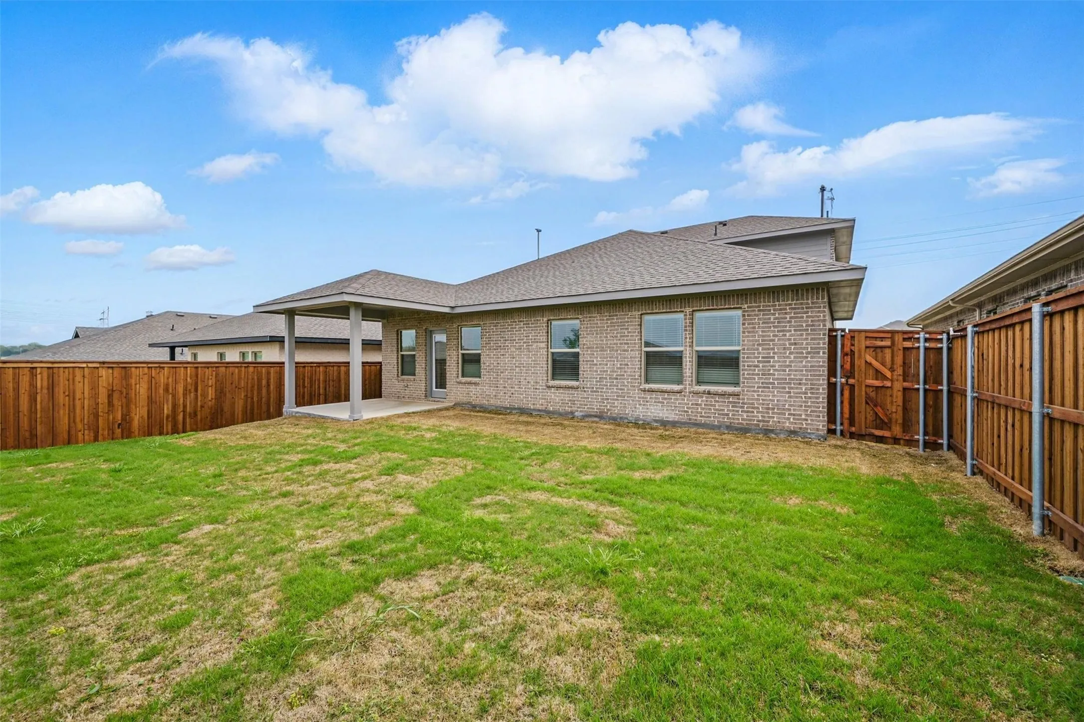 Expansive backyard featuring a covered patio, a full privacy fence, and a brick exterior