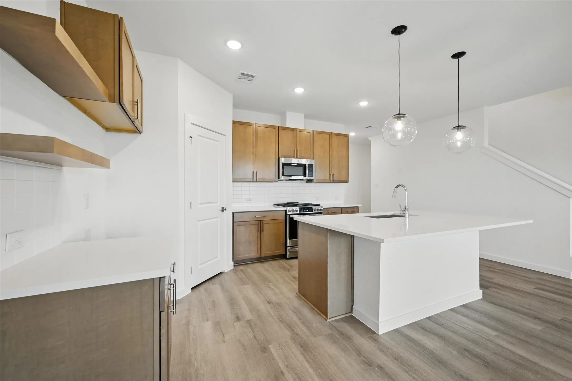 Open-concept kitchen featuring an oversized island with an undermount sink, pendant lighting, built-in stainless steel appliances, wood-finish cabinetry, and wood-finish flooring