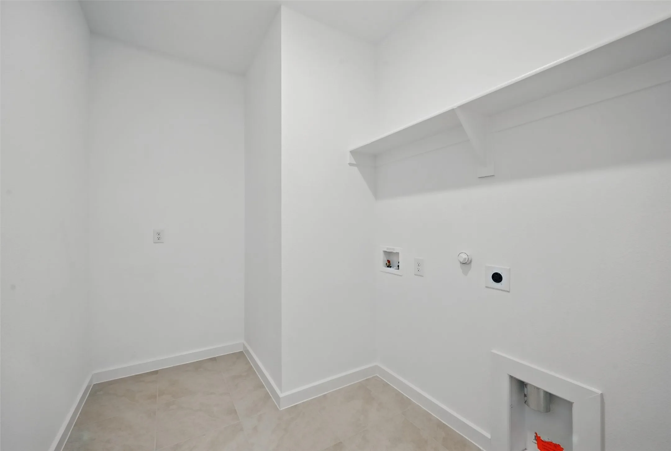 Dedicated utility space featuring a wall-mounted shelf, light-toned tile flooring, and white baseboards
