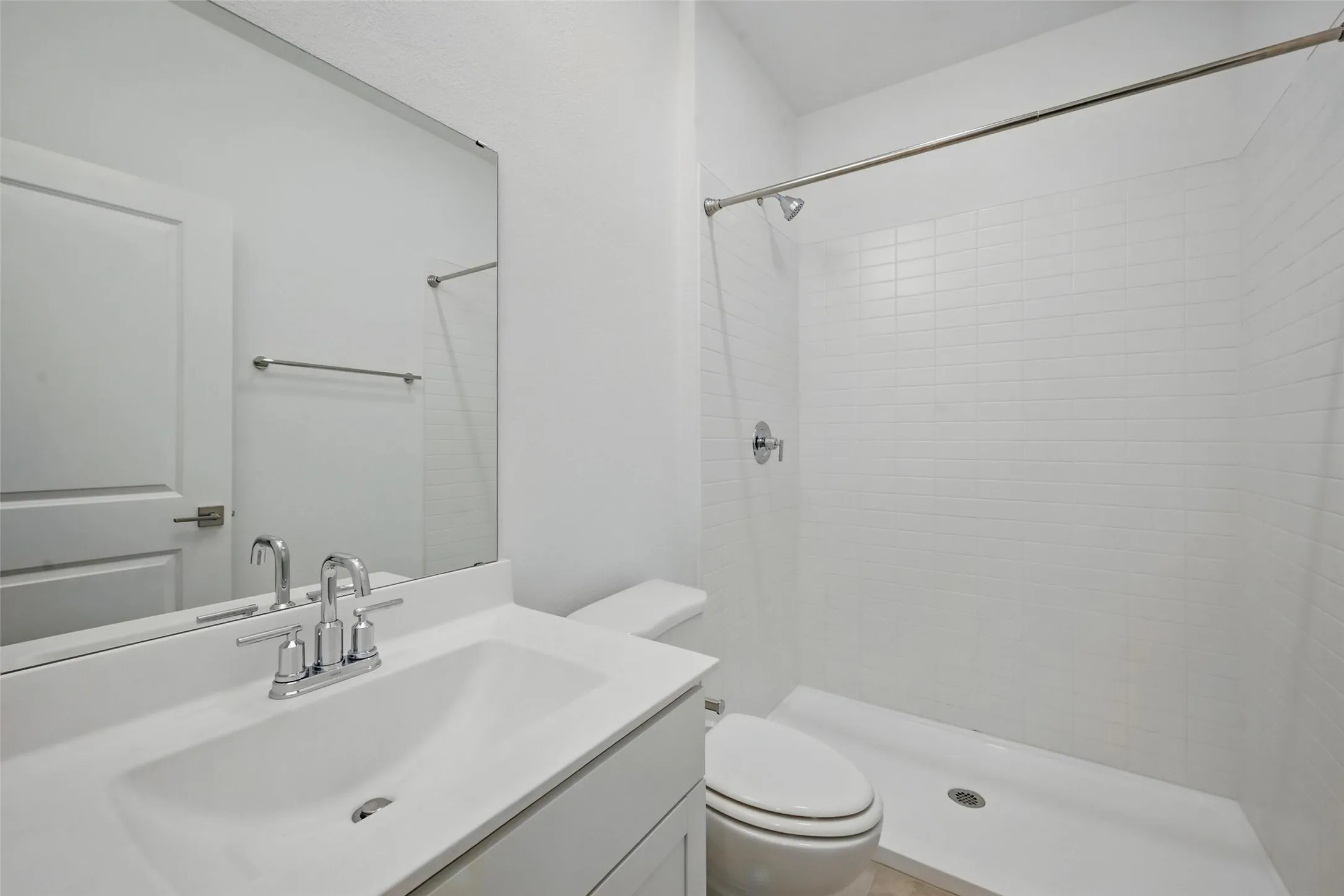 Bathroom featuring a white vanity with integrated sink, chrome faucet, frameless mirror, and a walk-in shower with white subway tile