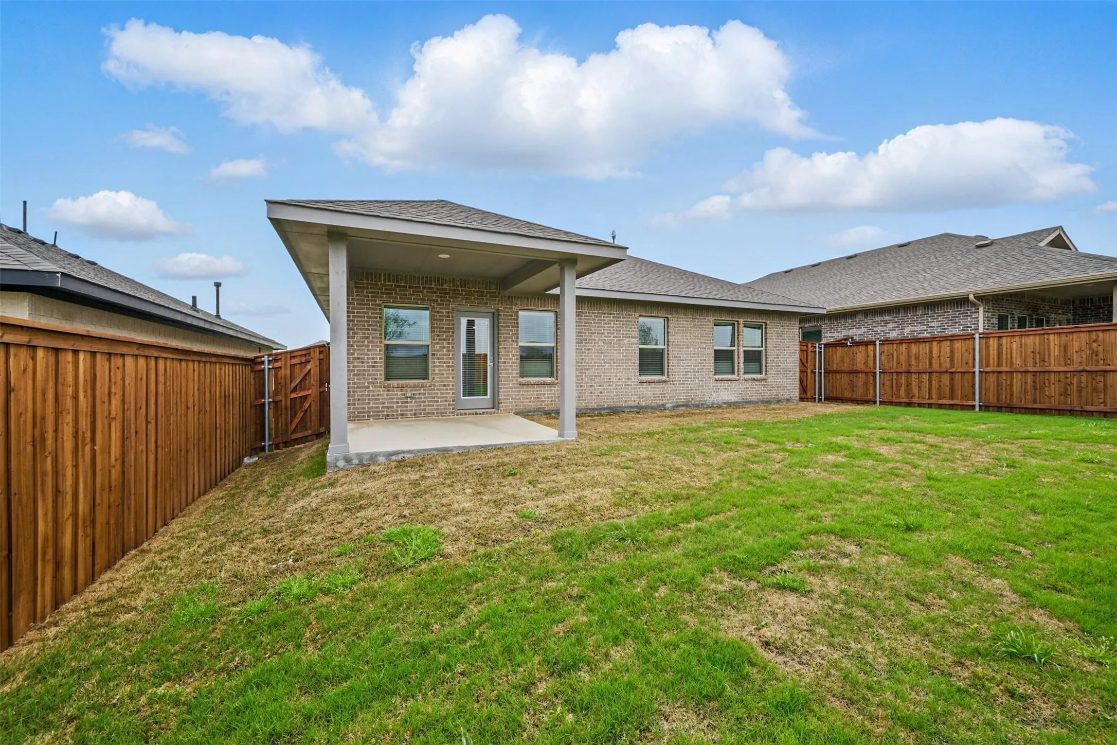 Expansive backyard featuring a covered concrete patio, full privacy fencing, brick exterior, and multiple windows