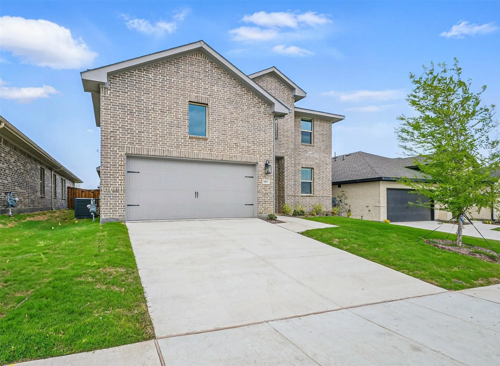 Brick facade residence featuring a two-car garage with decorative hardware, a concrete driveway, and manicured green lawns