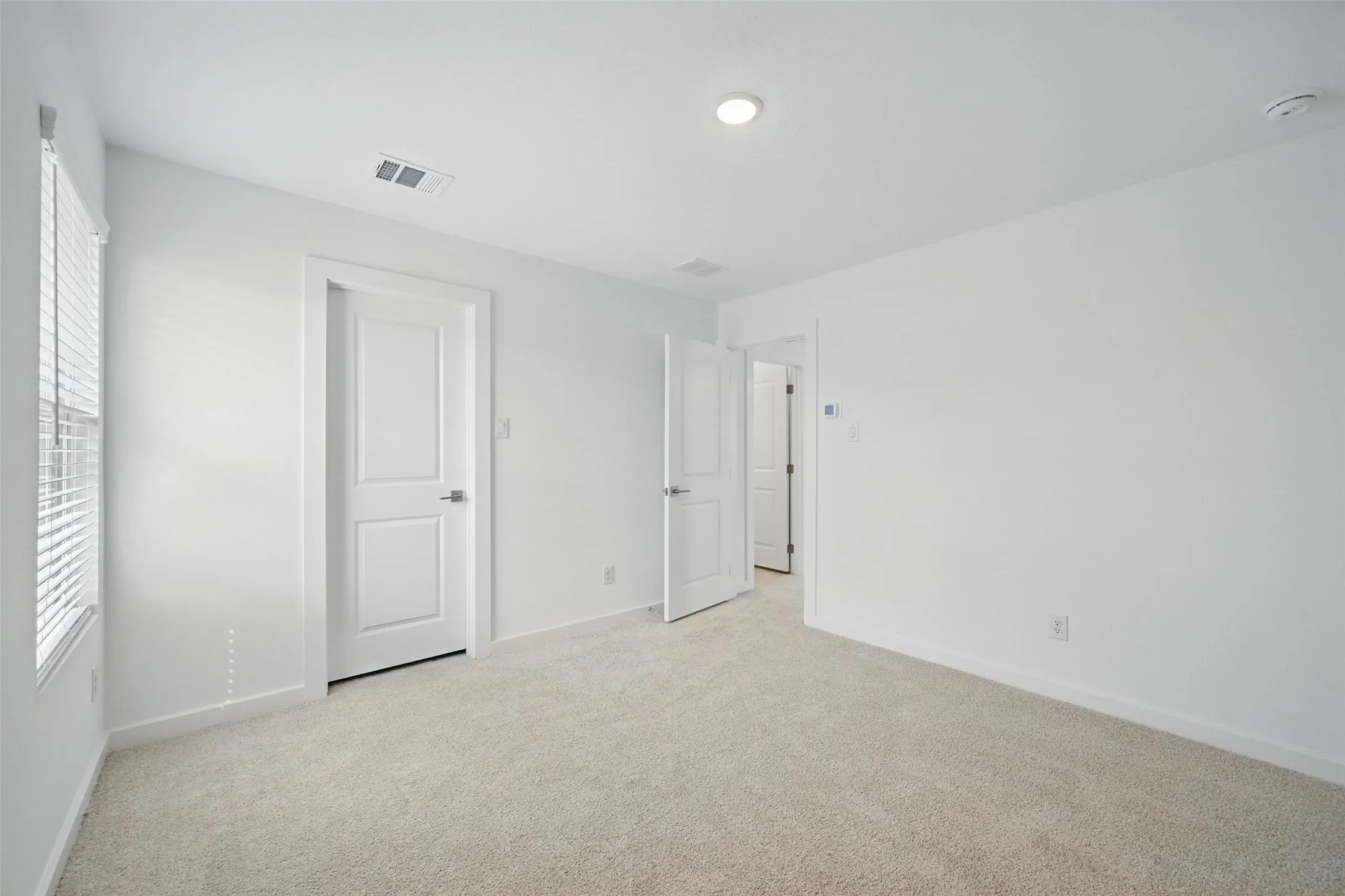 Neutral carpeted room with white walls, a single window with blinds, and recessed lighting