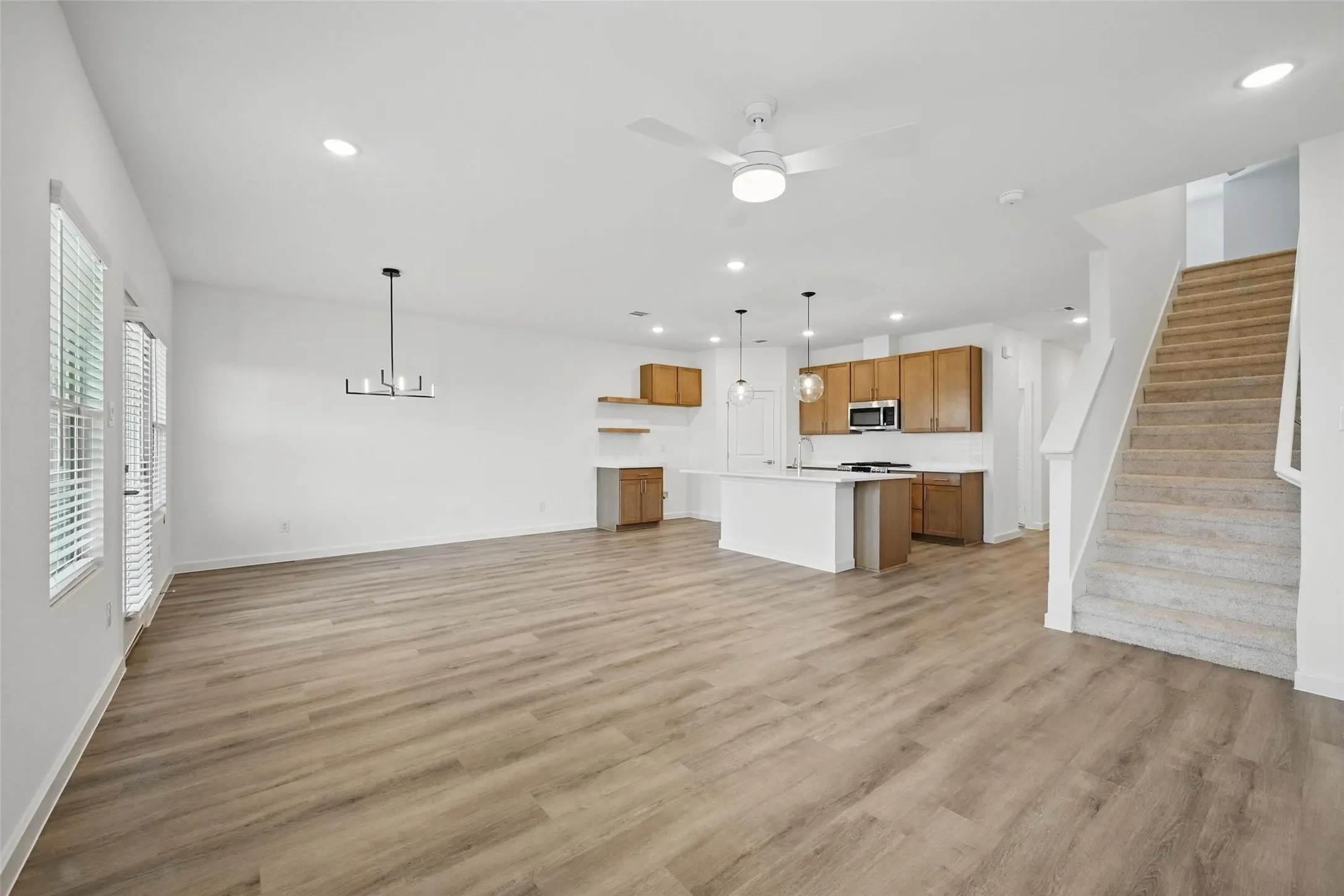 Open-concept living space featuring wood-finish flooring, a modern chandelier, and a ceiling fan