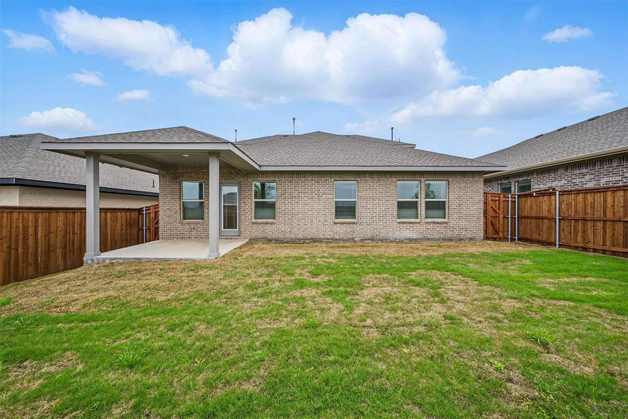 Rear exterior featuring a covered concrete patio, brick facade, and a wood privacy fence