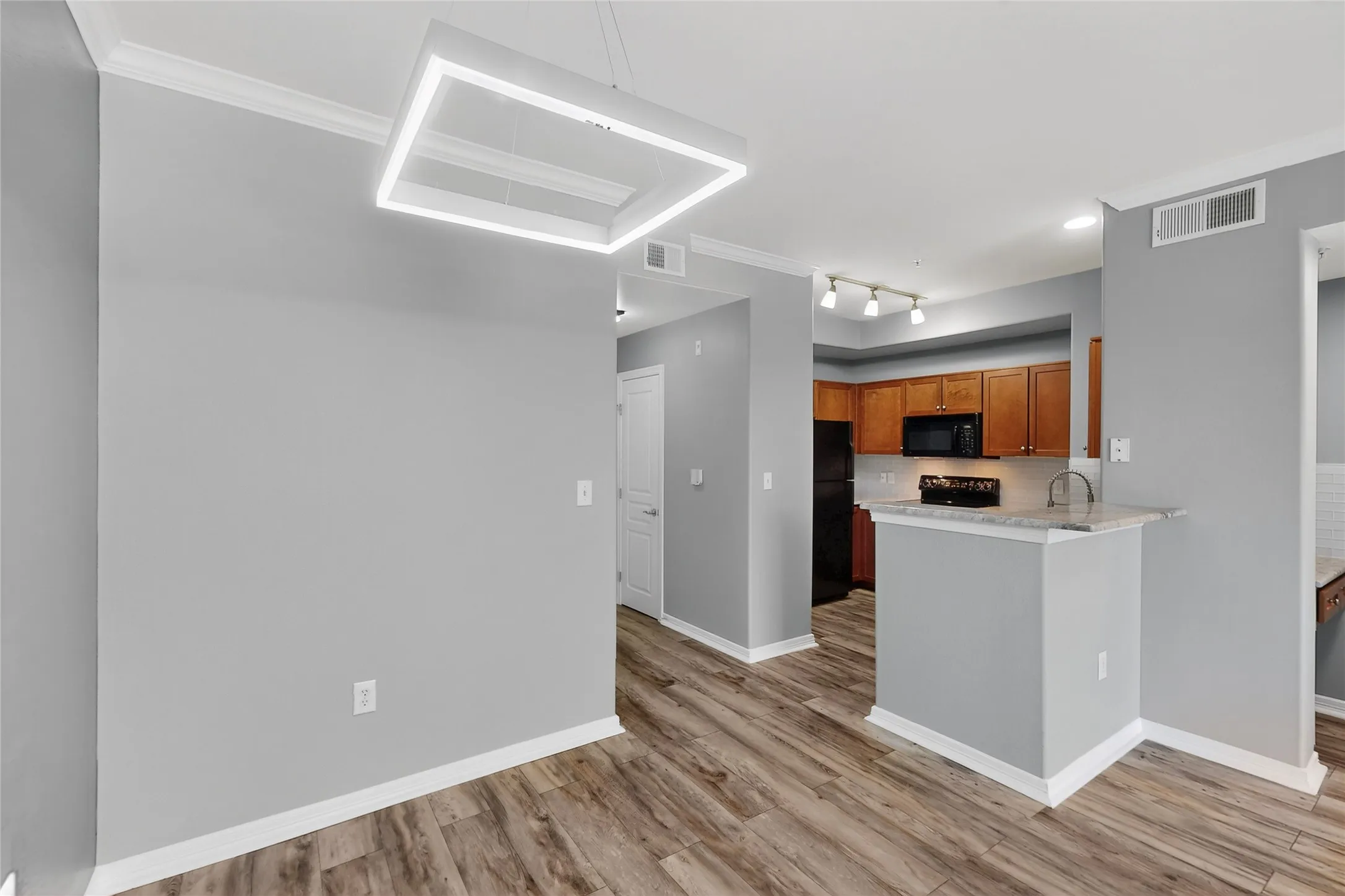Kitchen featuring brown cabinetry, light wood finished floors, a peninsula, light countertops, and crown molding