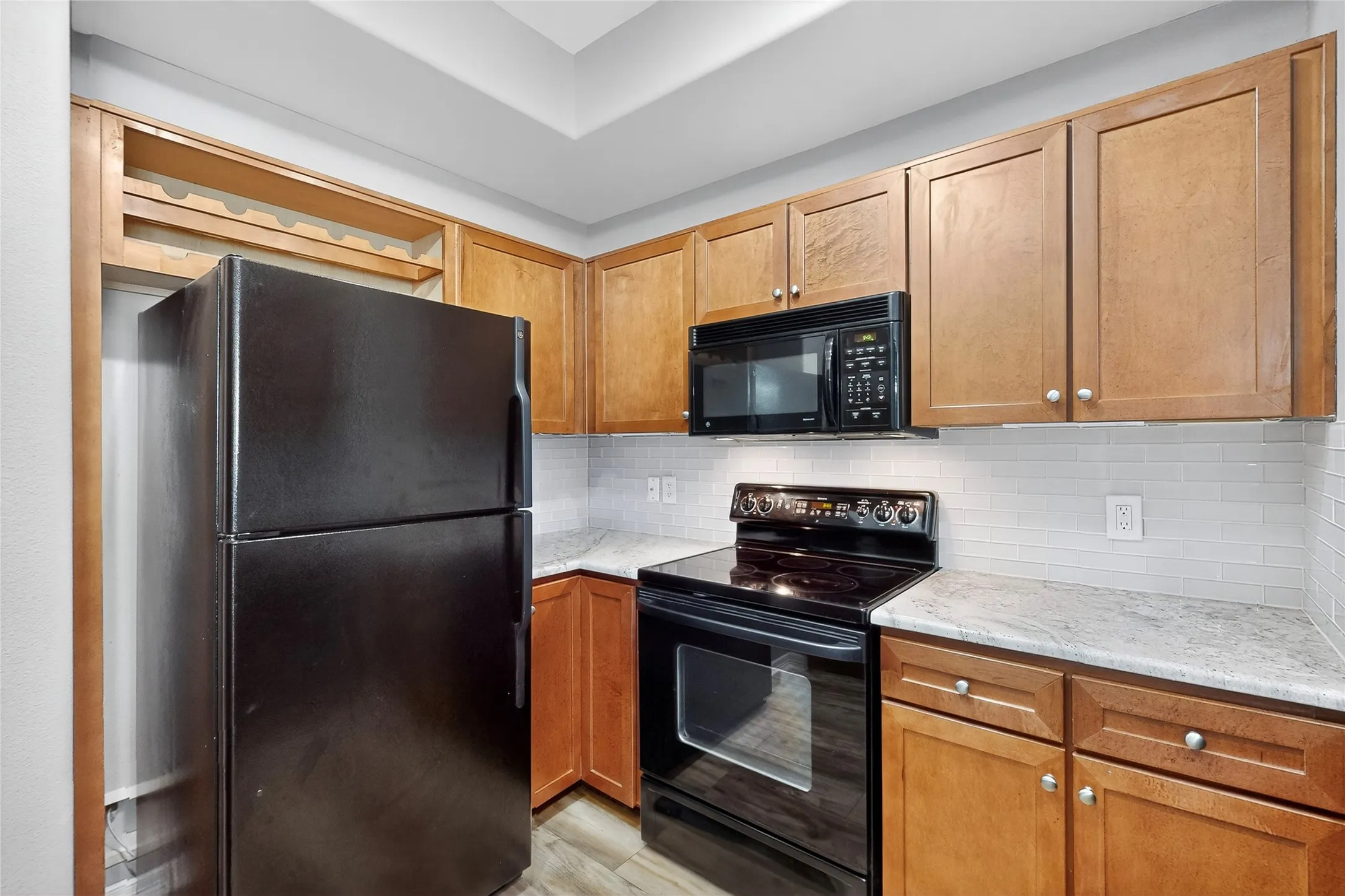 Kitchen featuring black appliances, light stone counters, backsplash, light wood-style floors, and brown cabinets